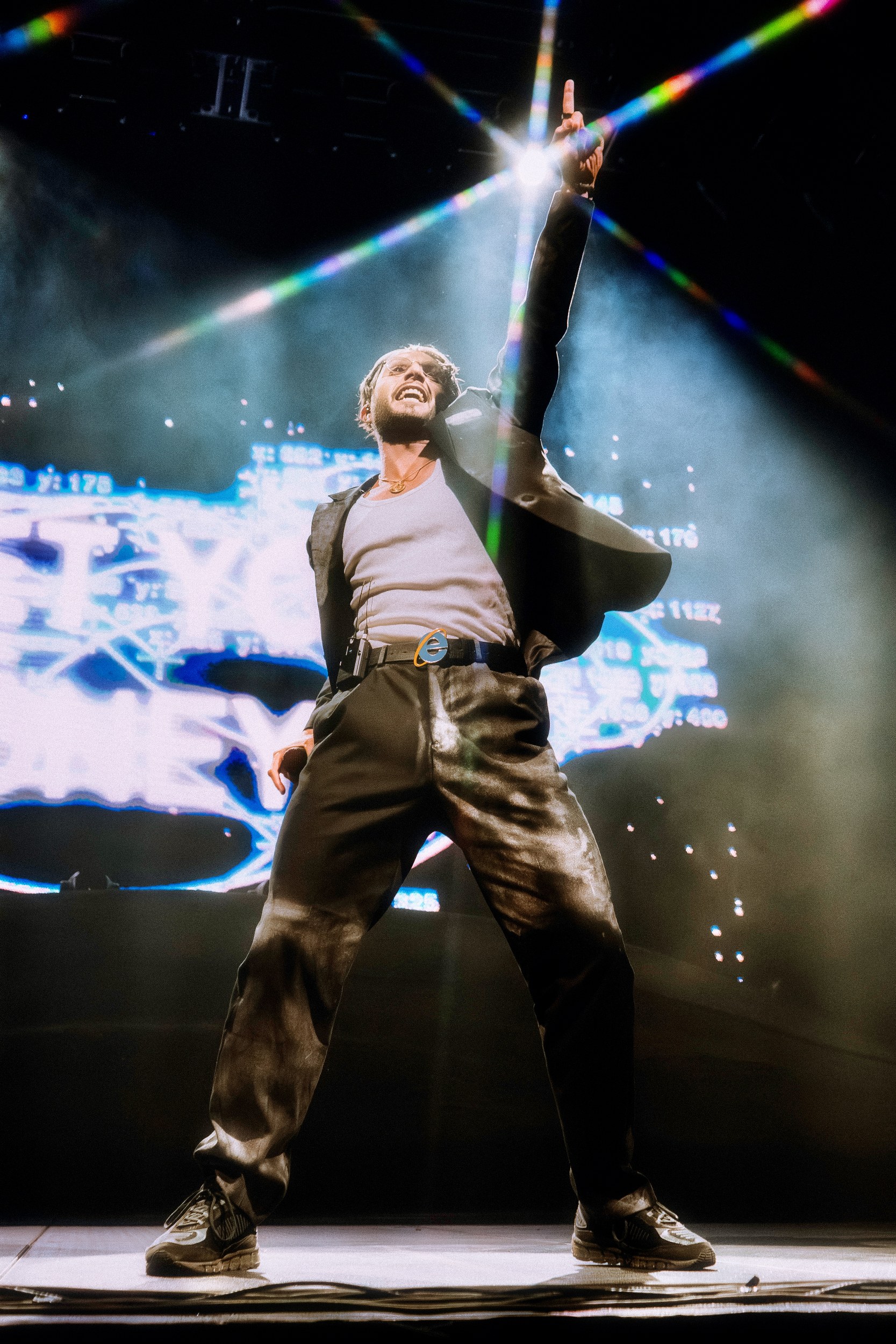 Performer on stage pointing upwards under colorful lights.
