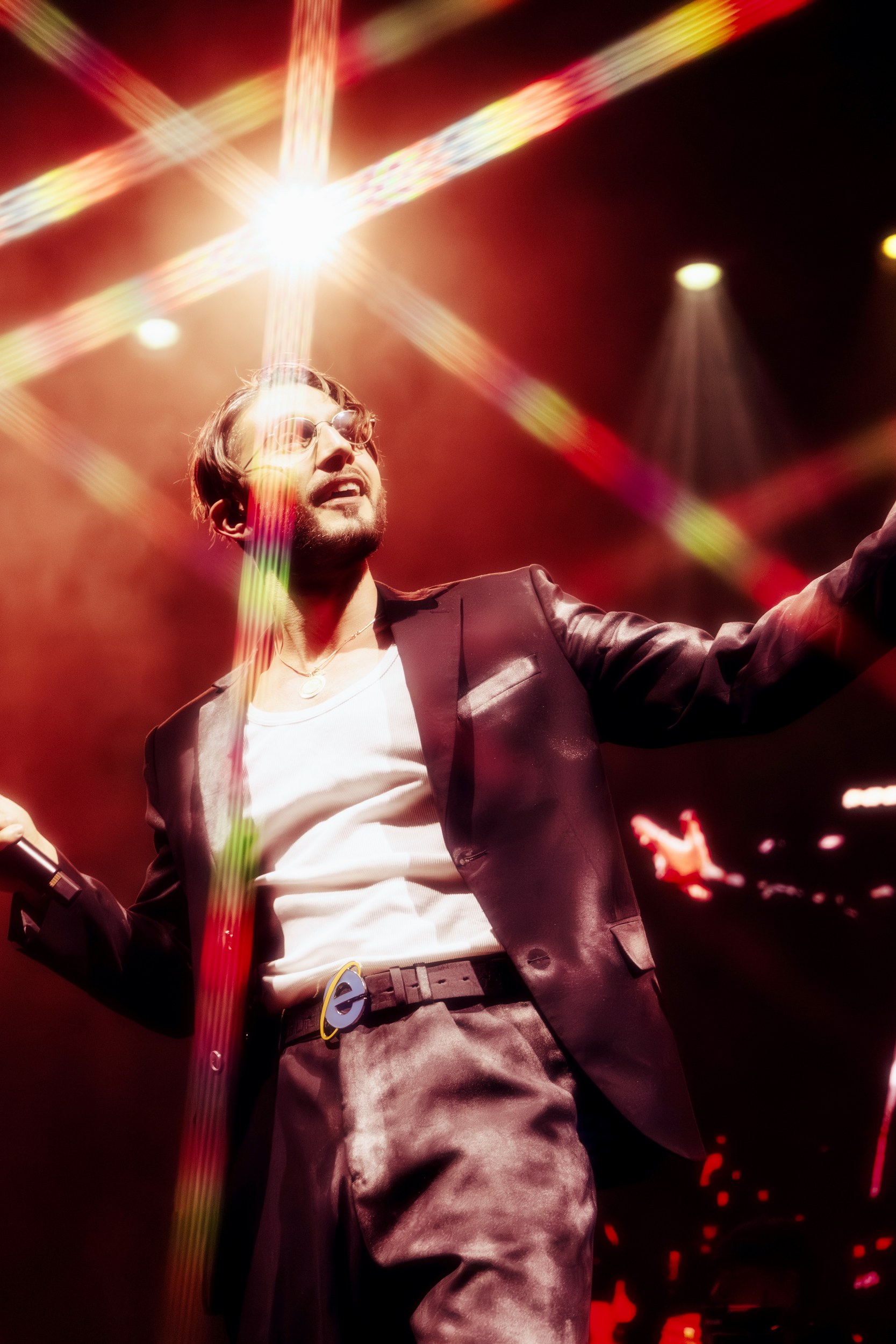 Performer in spotlight on stage, vibrant lights, singing passionately in a stylish outfit.