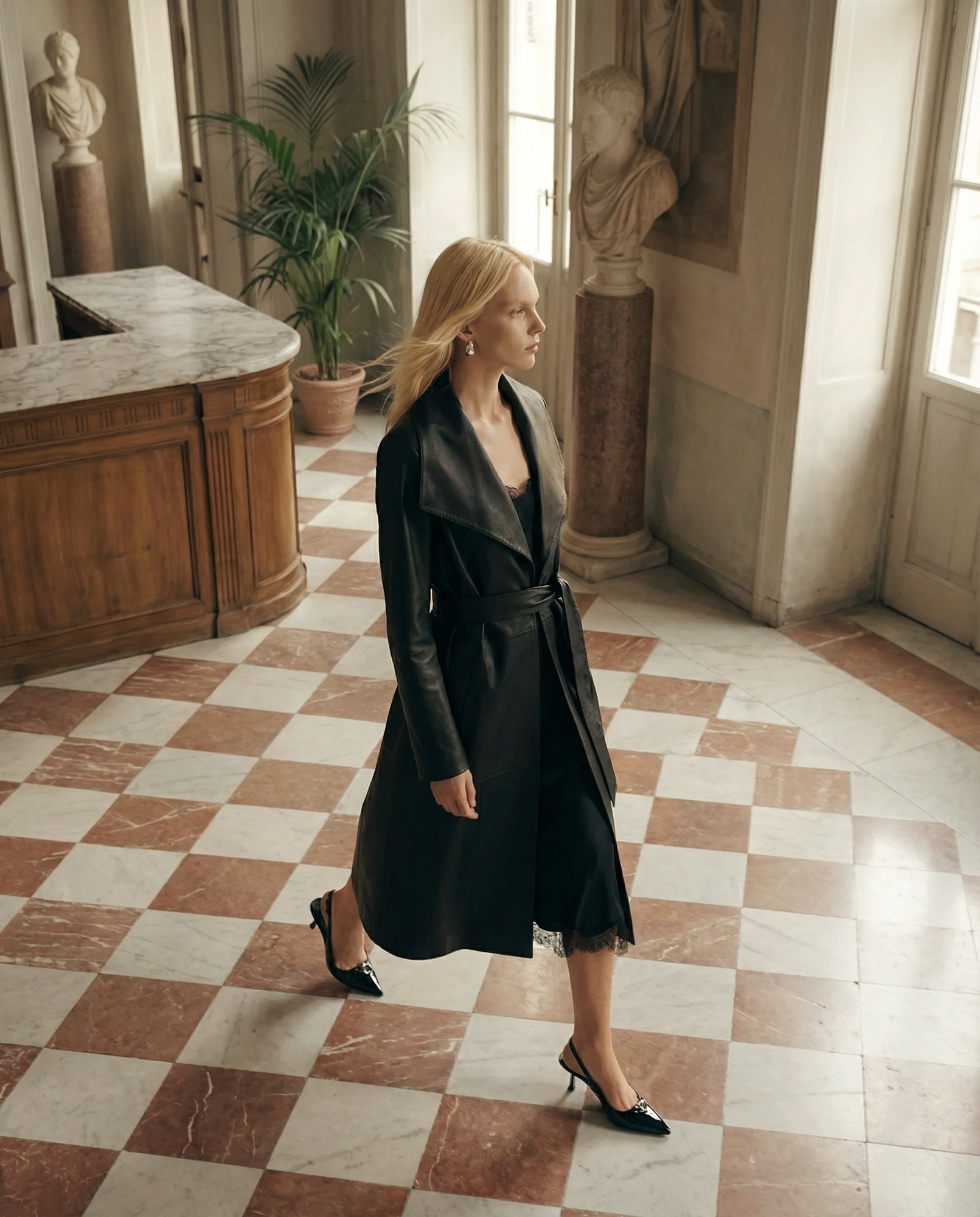 Elegant woman in black leather coat walking in checkered marble-floored room.