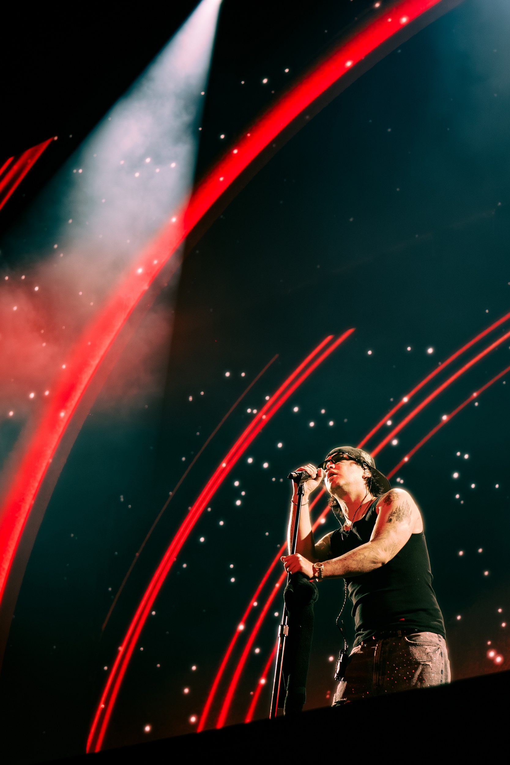 Rock singer performing live on stage with dramatic red lights and starry backdrop.