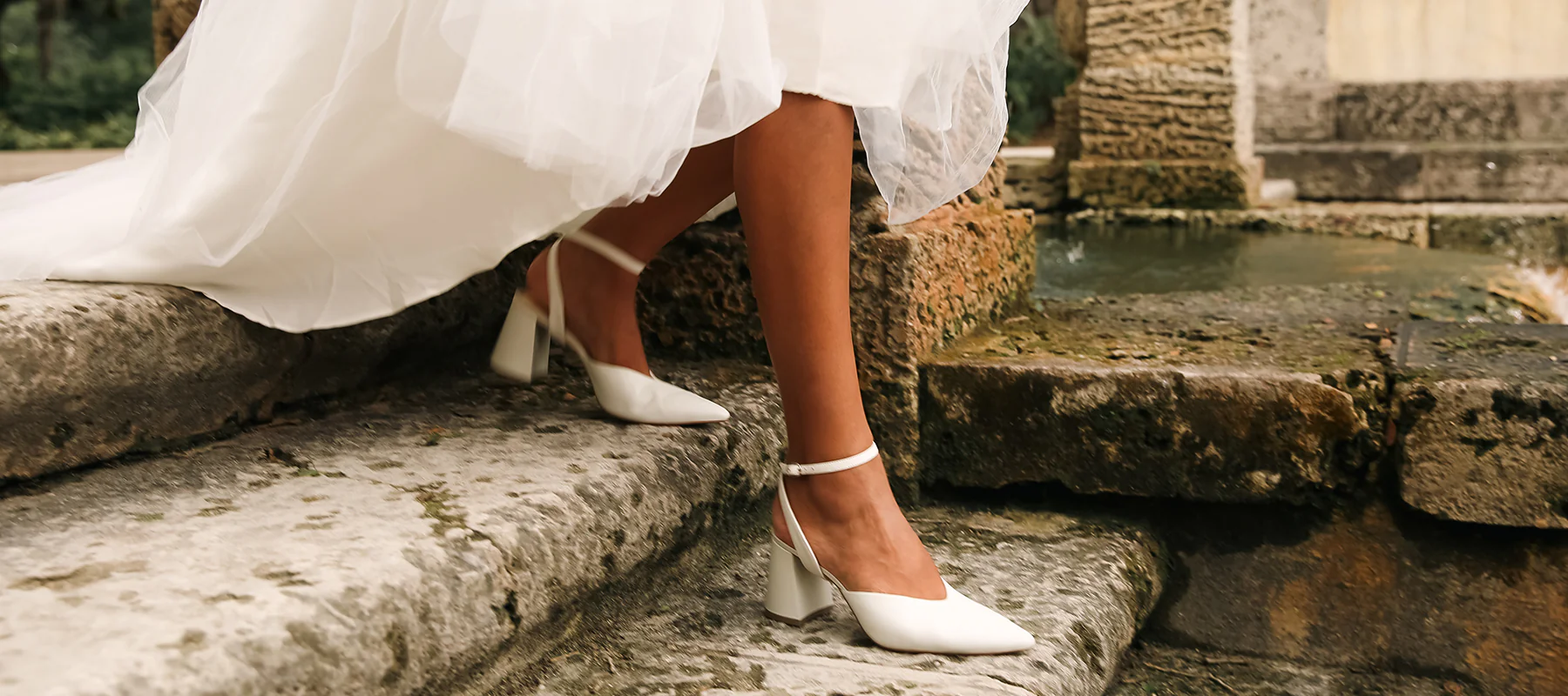 Bride stepping down stone stairs in elegant white heels and flowing wedding gown.