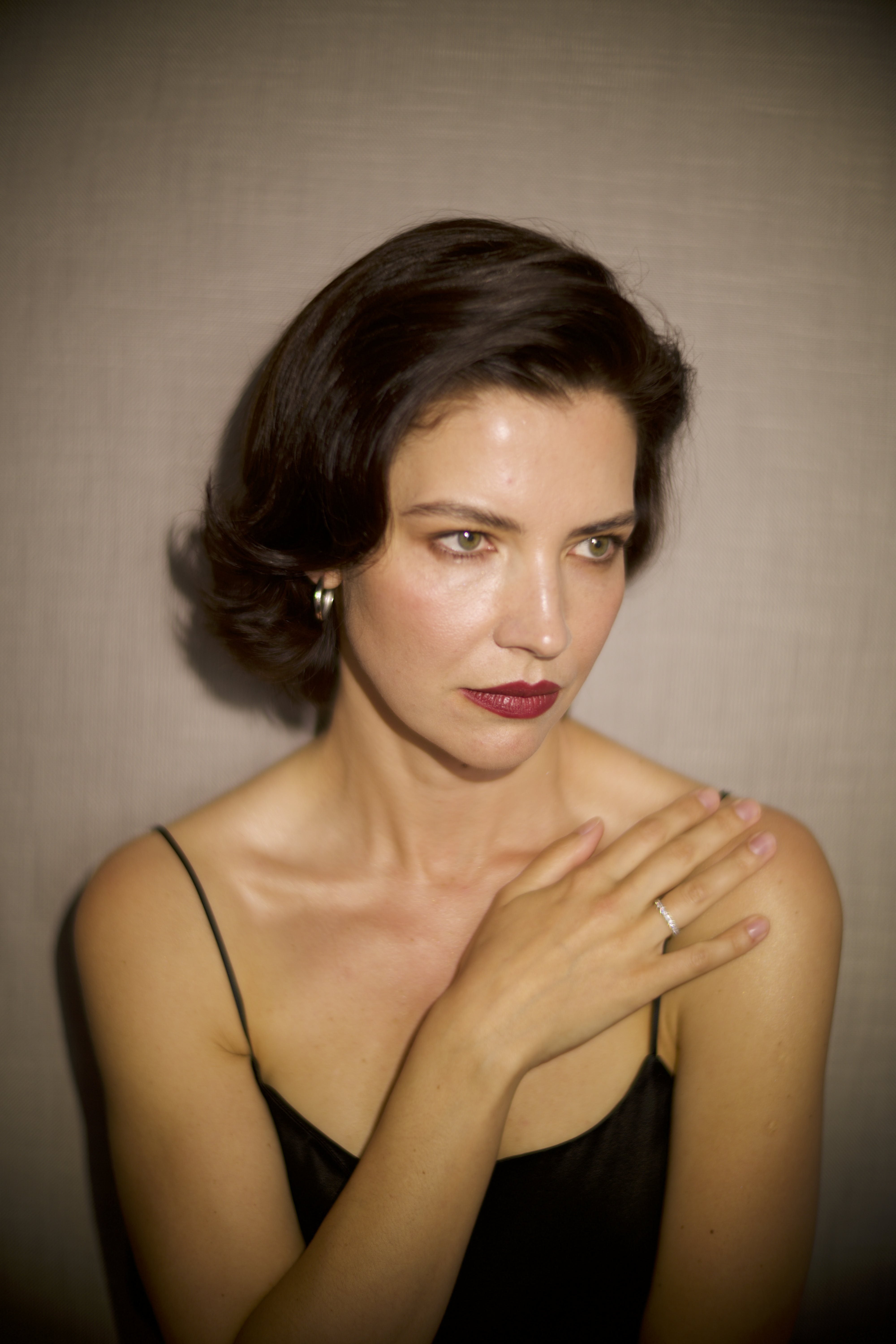 Woman in a black dress with shoulder-length hair, hand on shoulder, elegant expression.