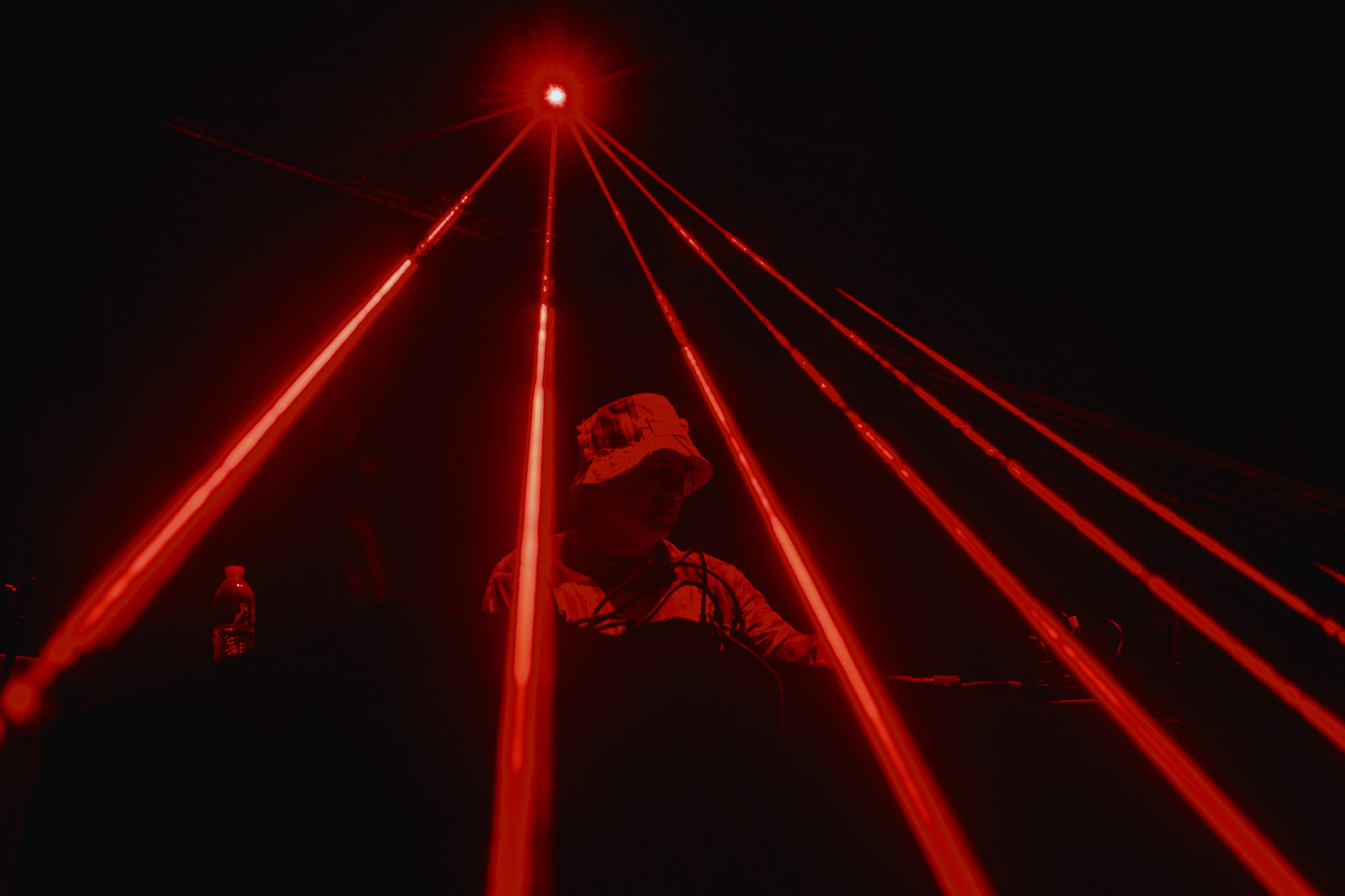 DJ performing under vivid red laser lights at a dark music event.
