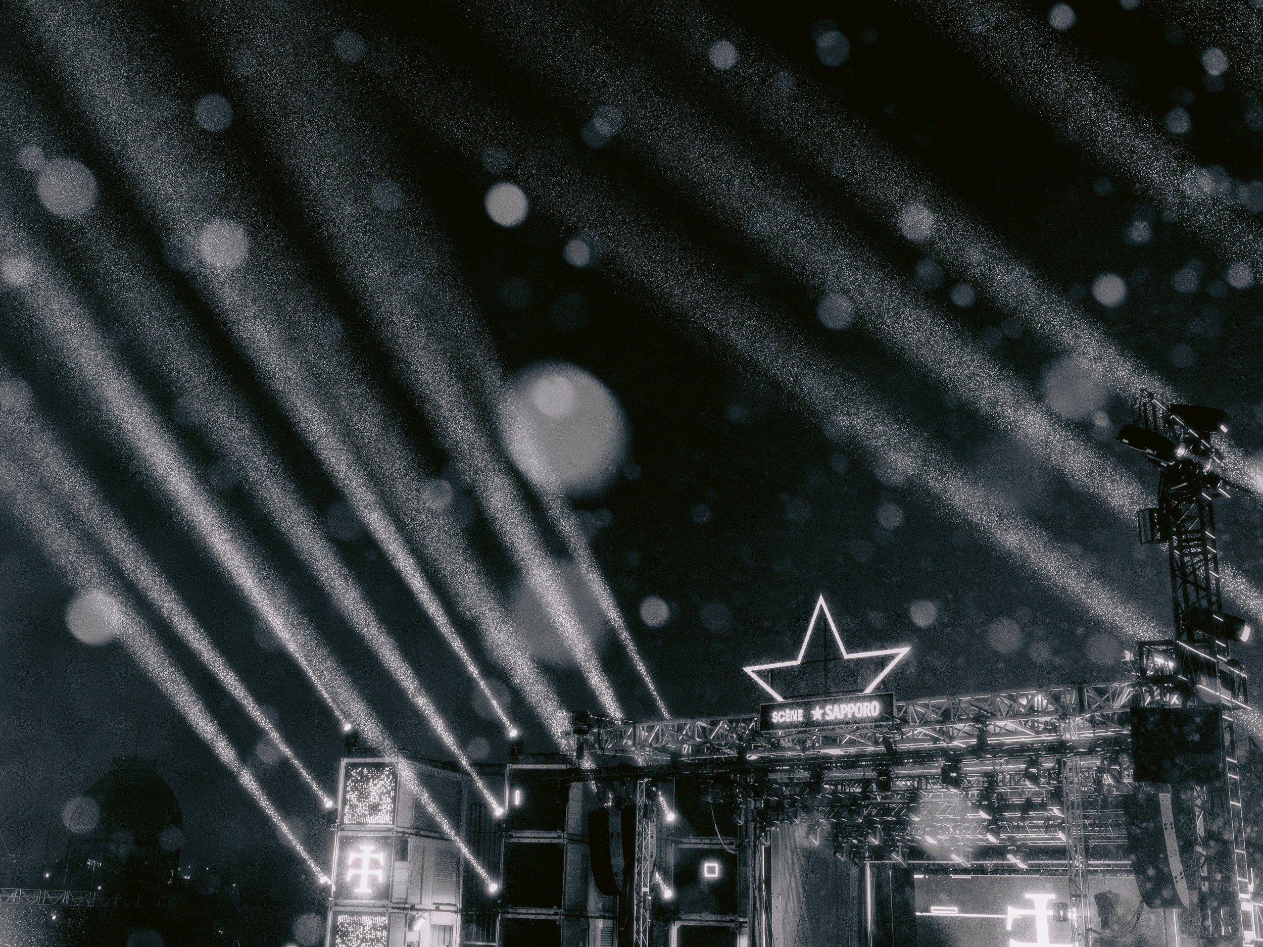 Outdoor concert stage with dramatic night lighting beams.
