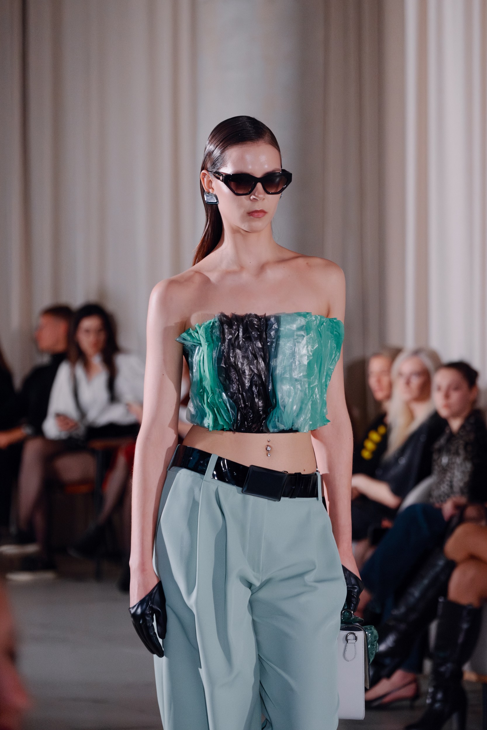 Model on runway in chic fashion ensemble, green top, light-blue pants.