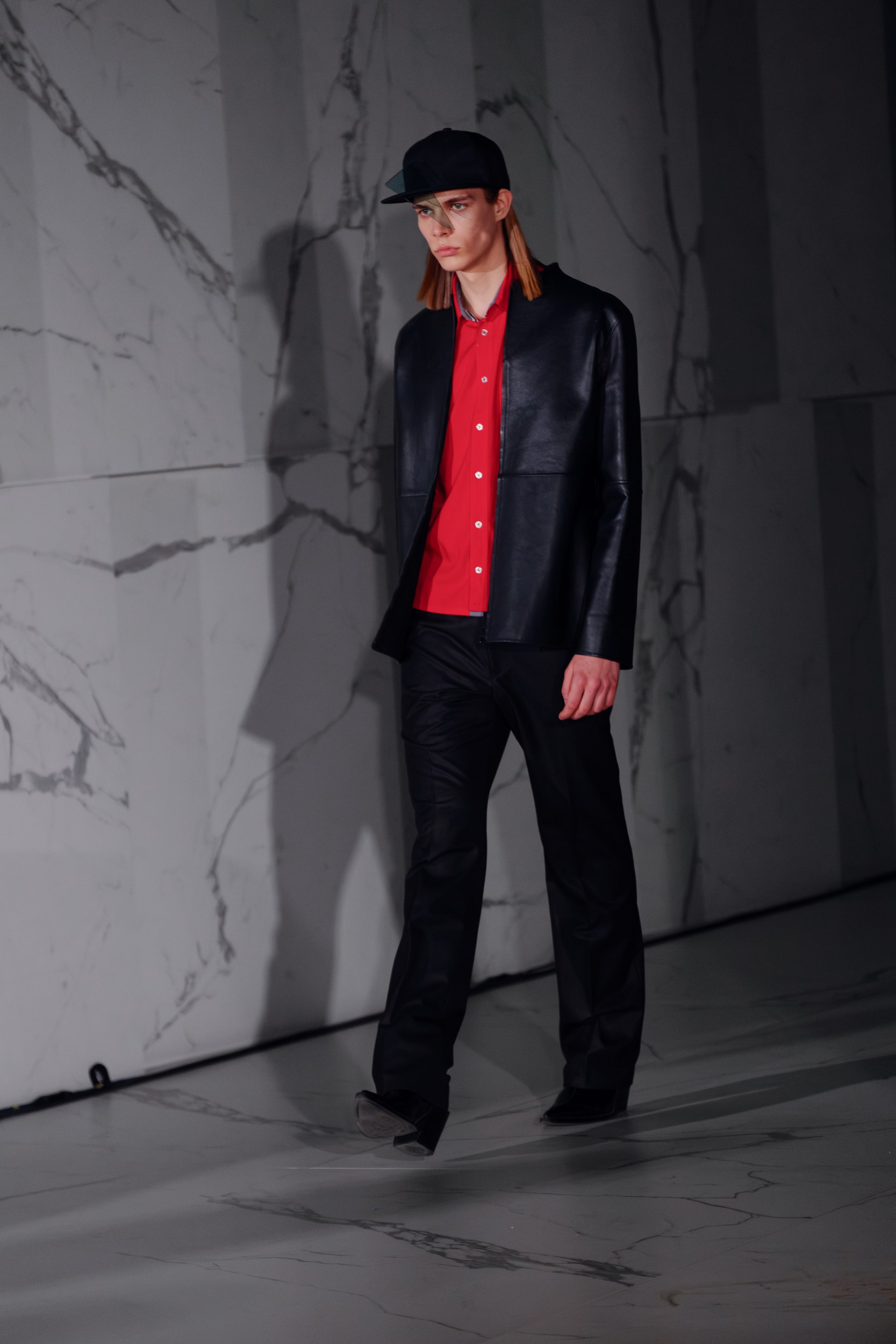 Model walking runway in stylish black and red fashion outfit, sleek modern look.