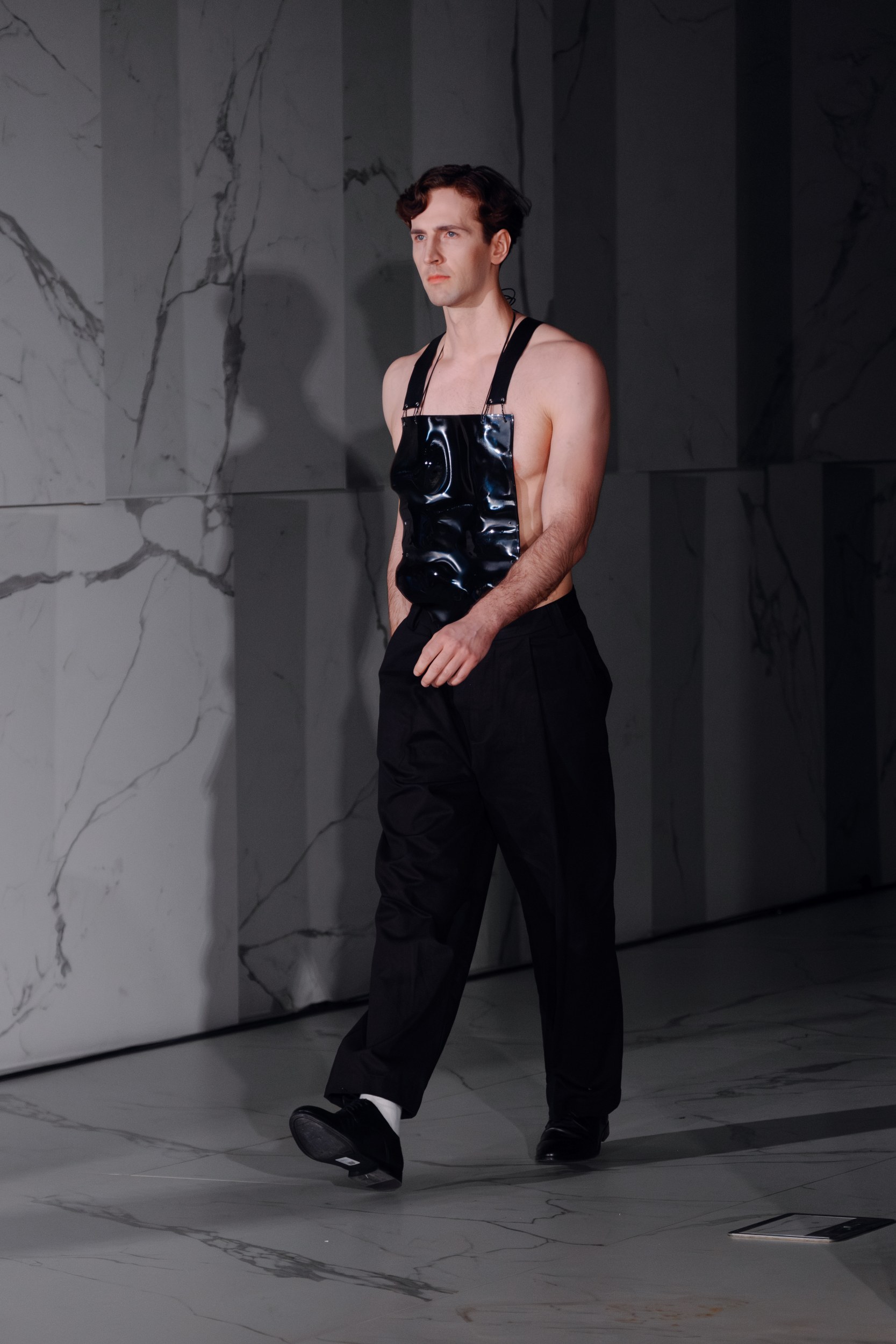 Model in black trousers and avant-garde top walking on a marble floor.
