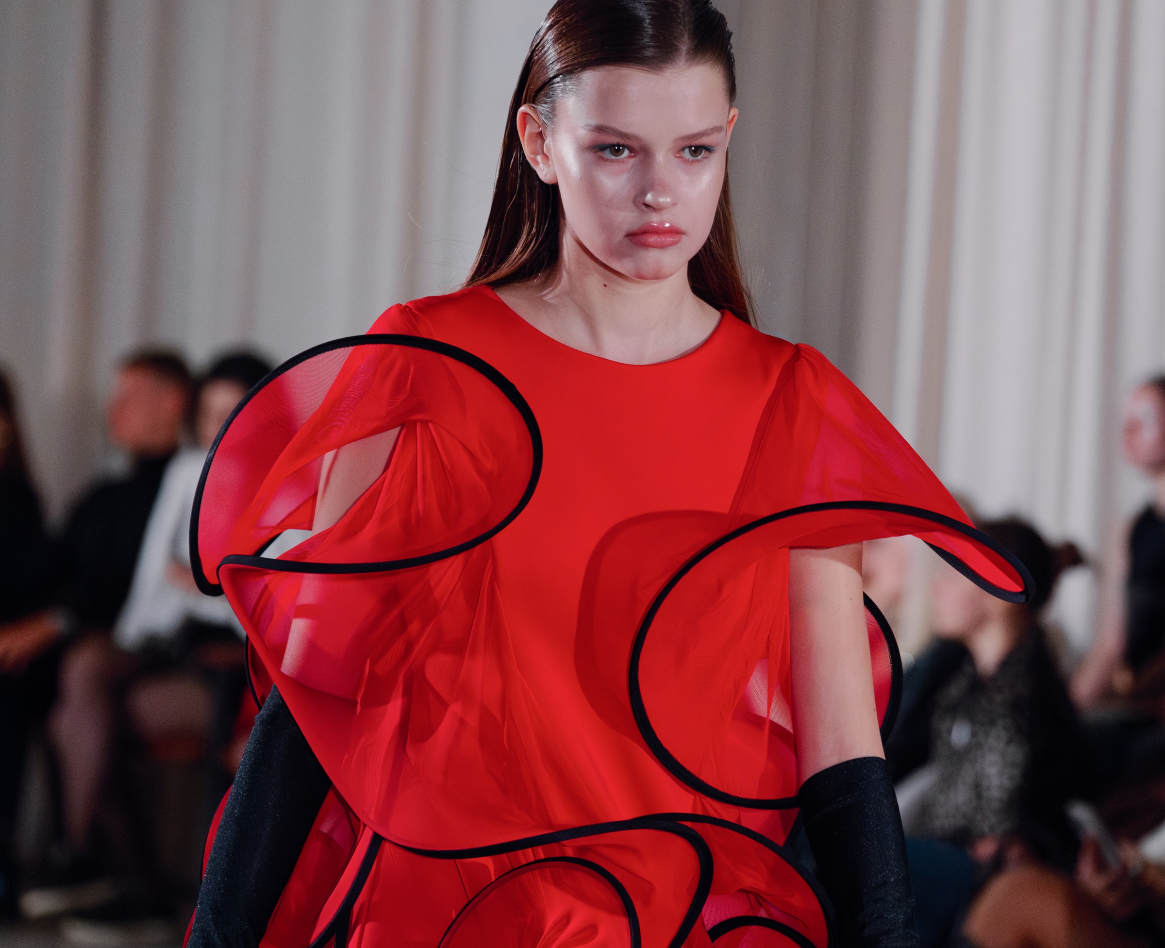 Model in vibrant red avant-garde dress on runway.