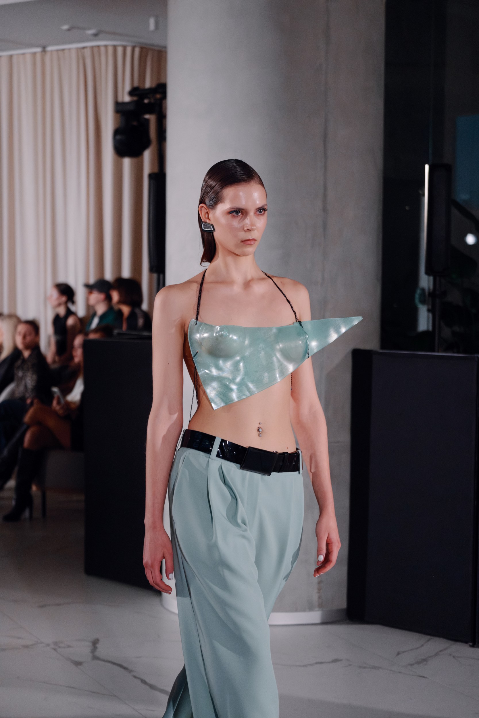 Model in futuristic fashion walks runway in metallic top and flowing trousers.