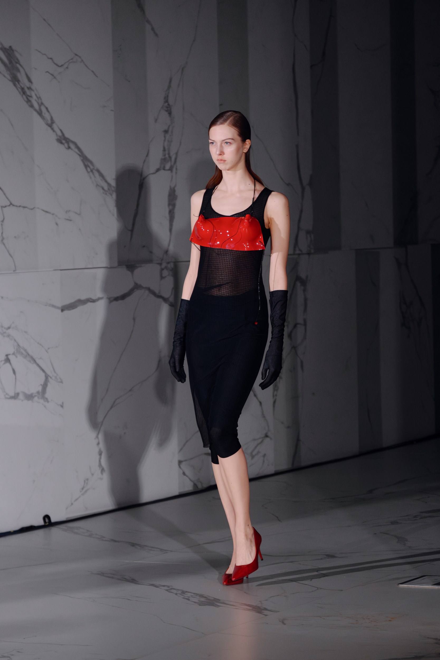Model in a chic black and red dress on marble runway. Fashion show 2023.