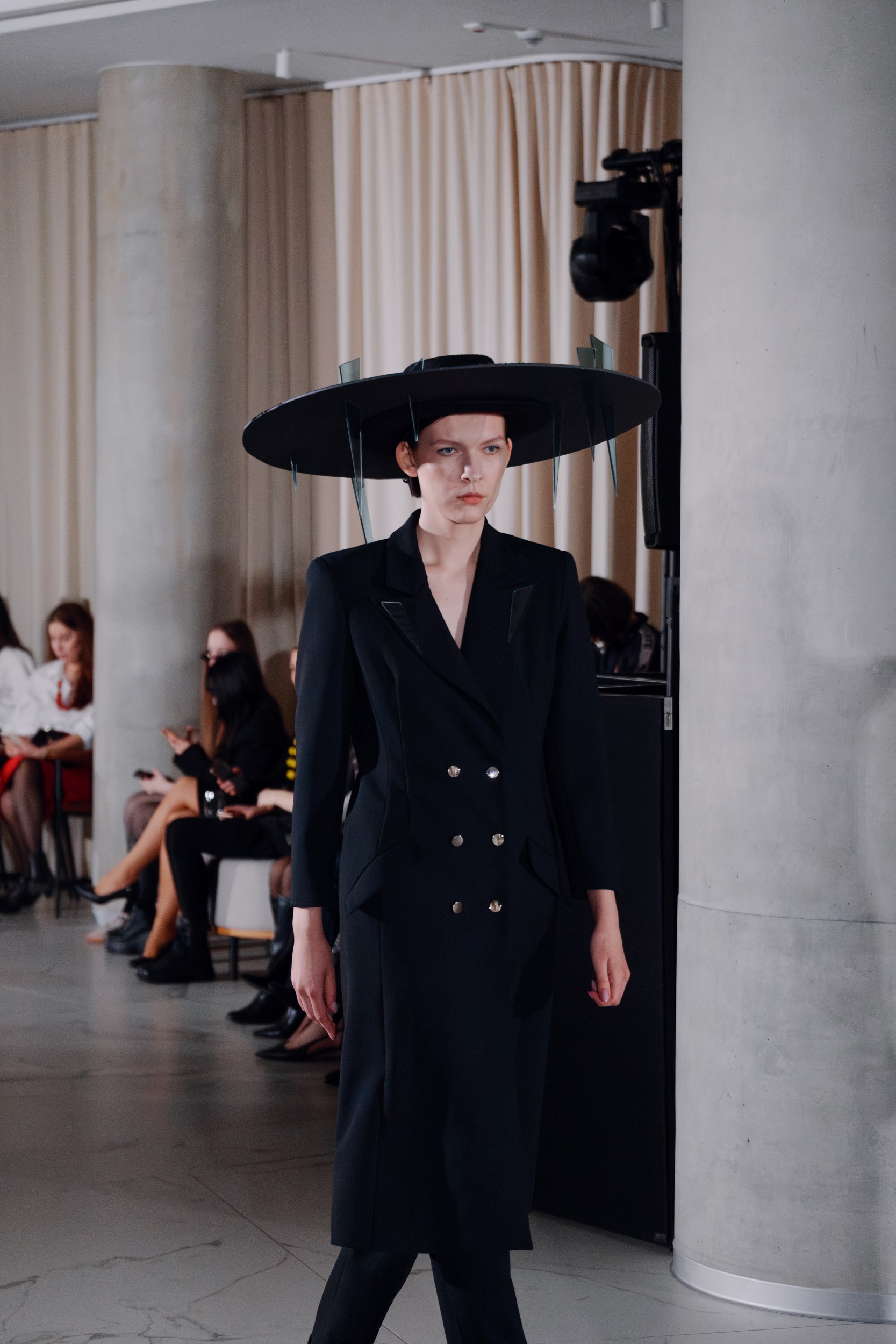Model in avant-garde fashion with wide-brimmed hat on a runway.