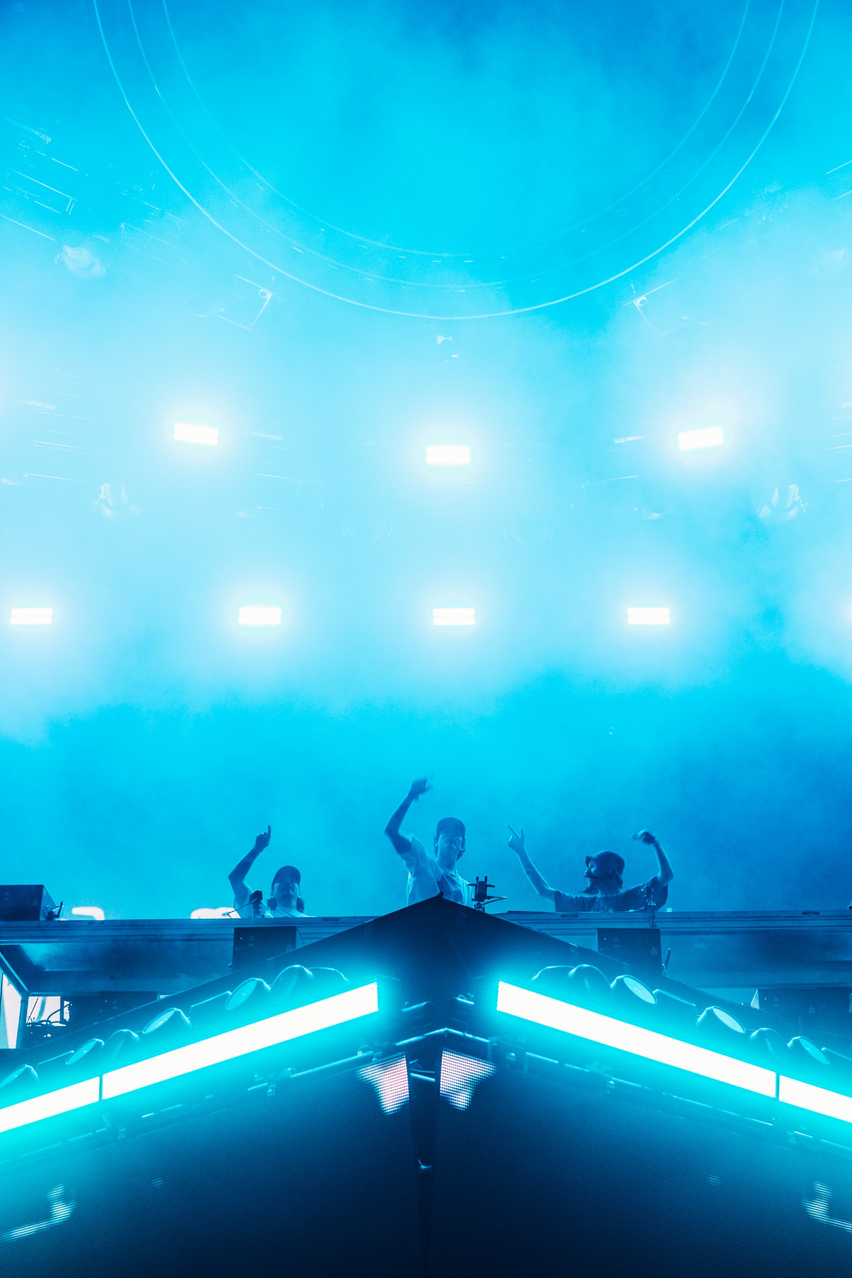DJ trio performing on a vibrant stage with blue lights and fog.