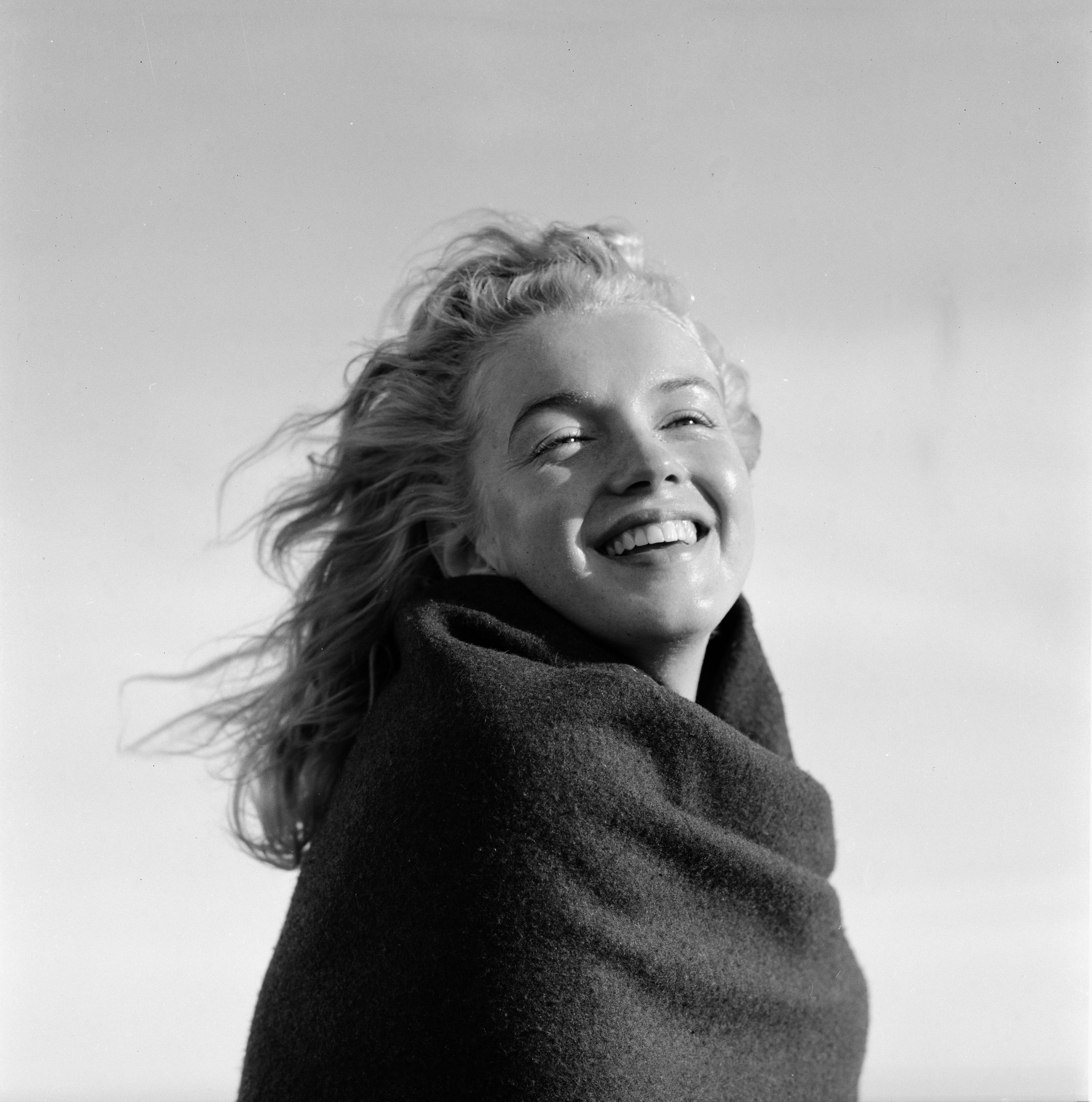 Smiling woman wrapped in a blanket, enjoying a windy day outdoors.