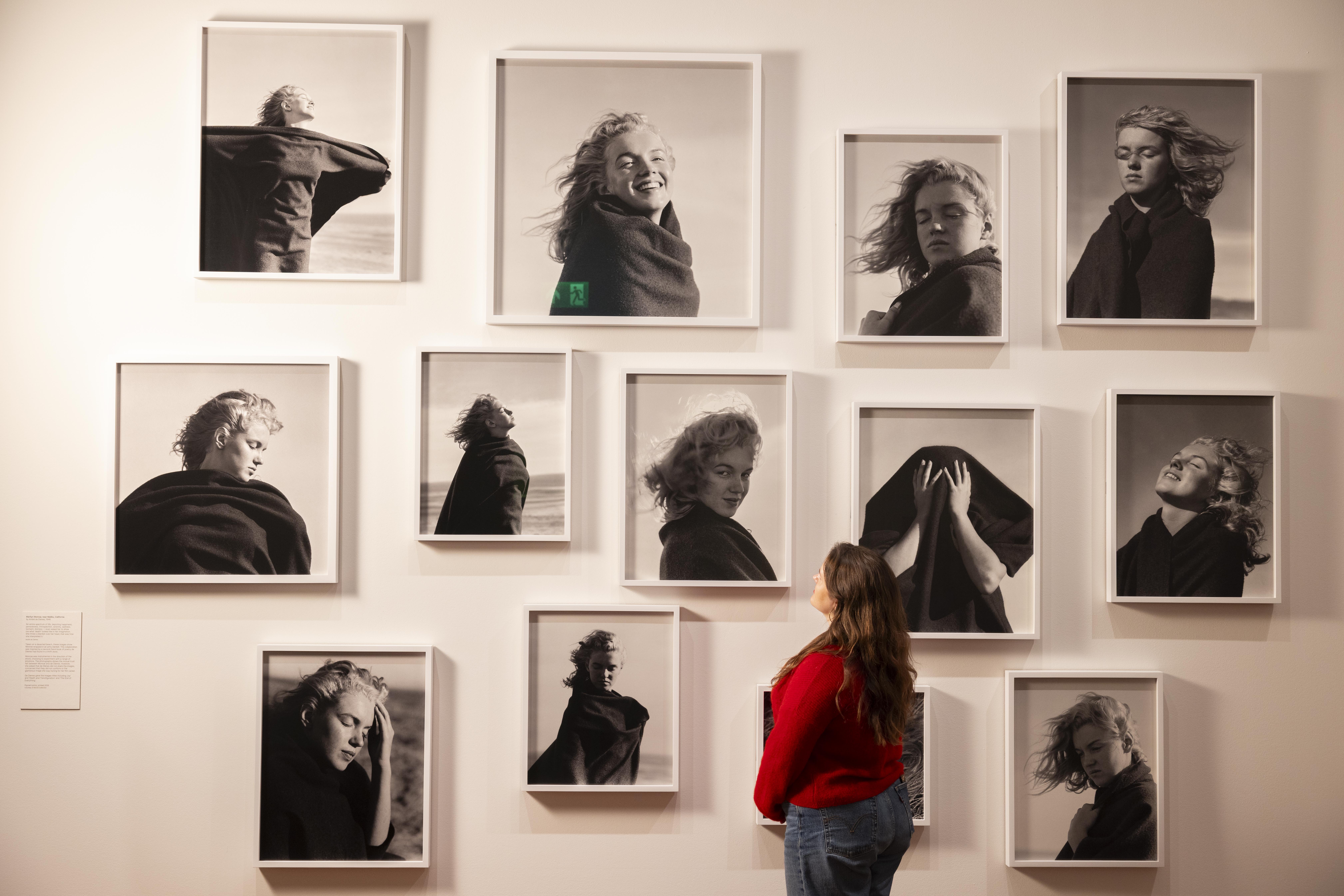 Woman observes a gallery wall filled with black-and-white portraits in a museum.