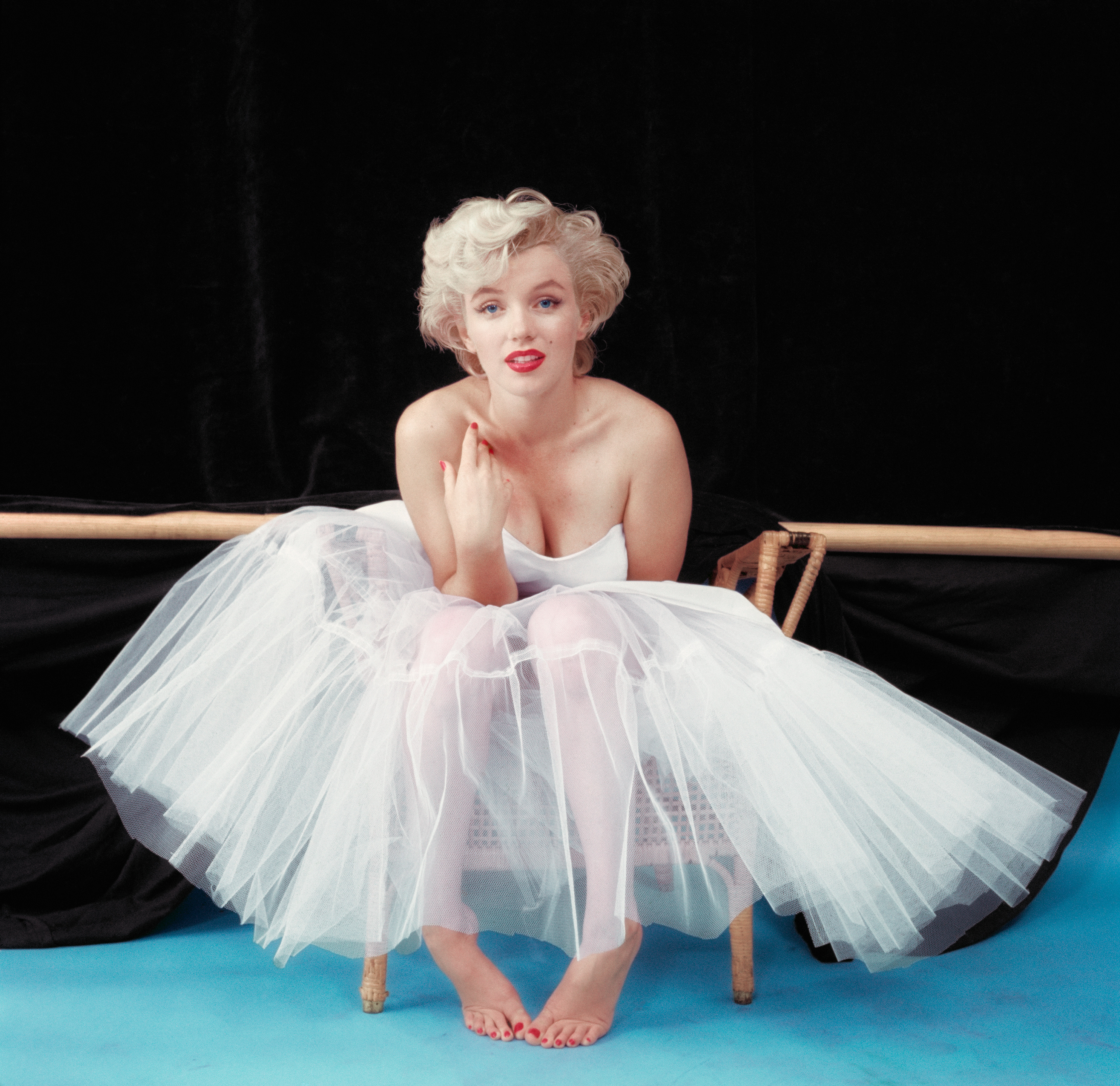 Person in a white dress sitting elegantly on a chair with a black background.