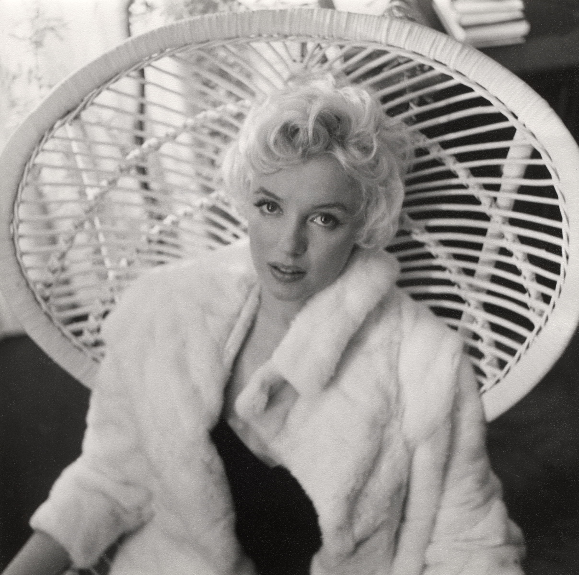 Black-and-white portrait of a woman in a fur coat sitting in a wicker chair.