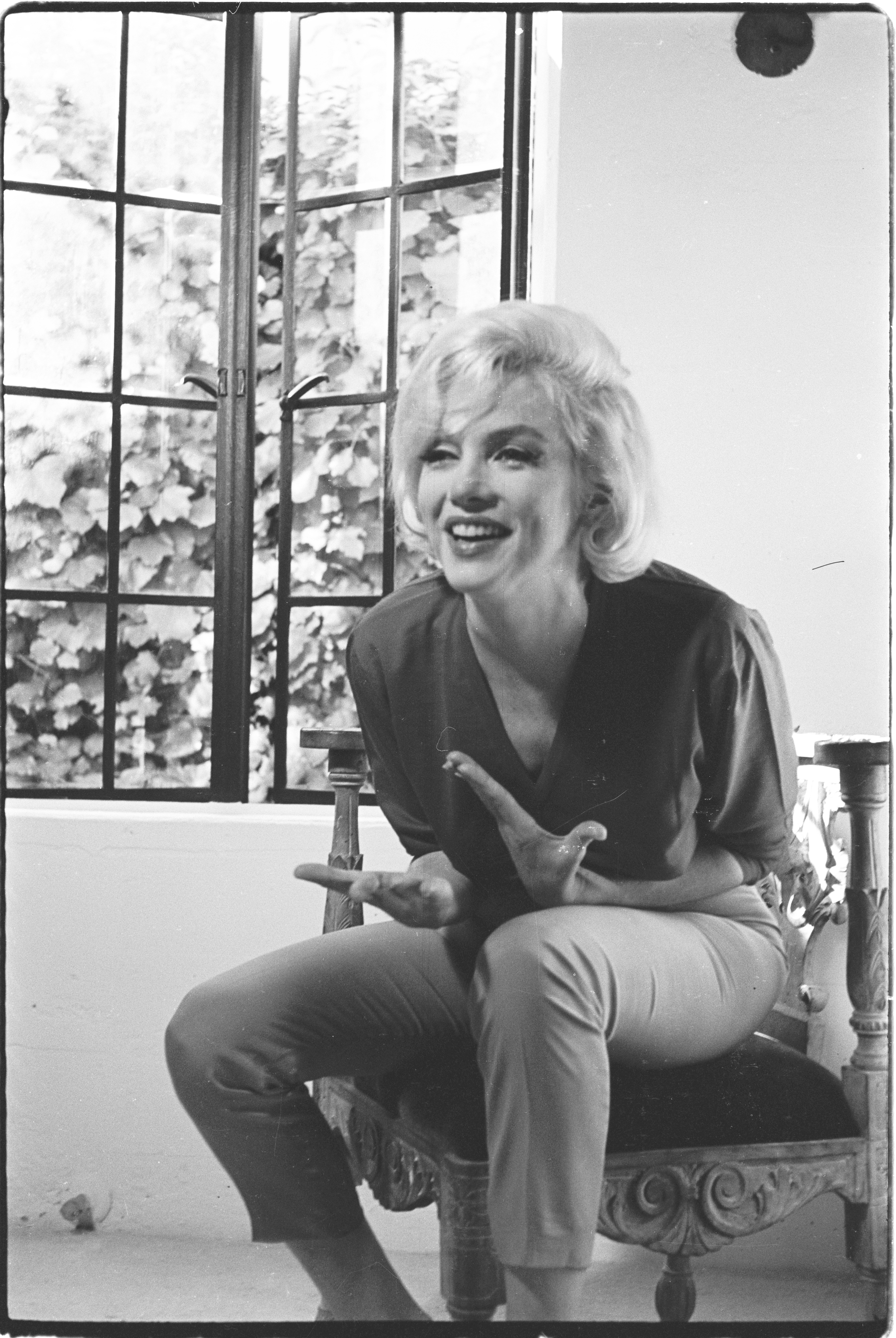 Smiling woman in retro outfit sitting by a window, sharing a joyful moment.