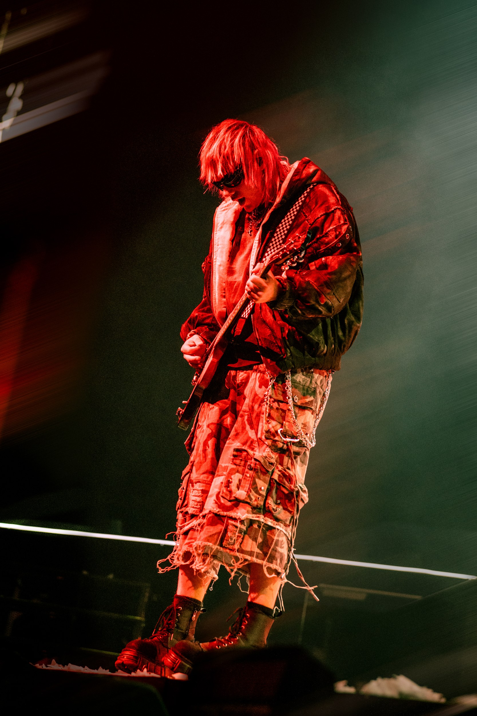 Guitarist performing on stage in vibrant red lighting with dynamic style.