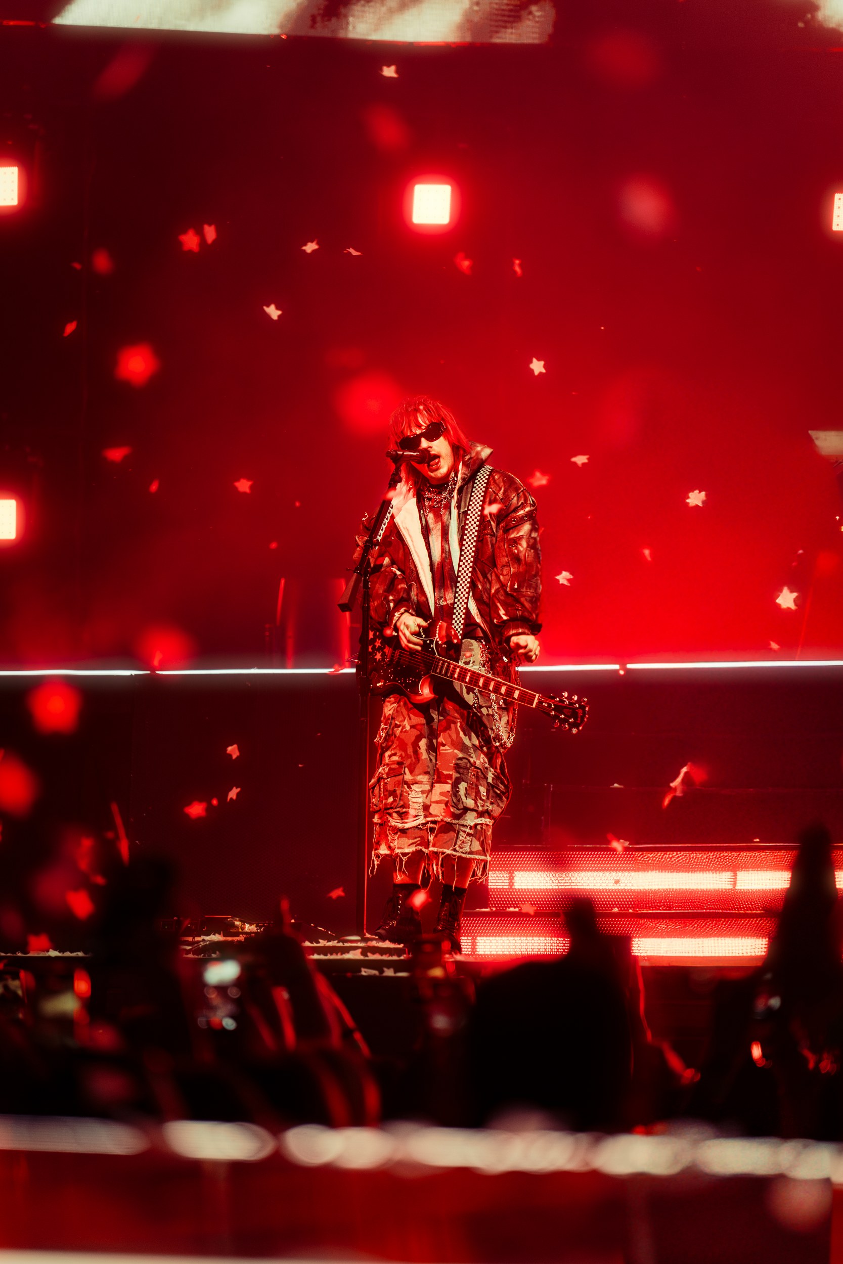 Rock musician performs onstage under red lights and star confetti.