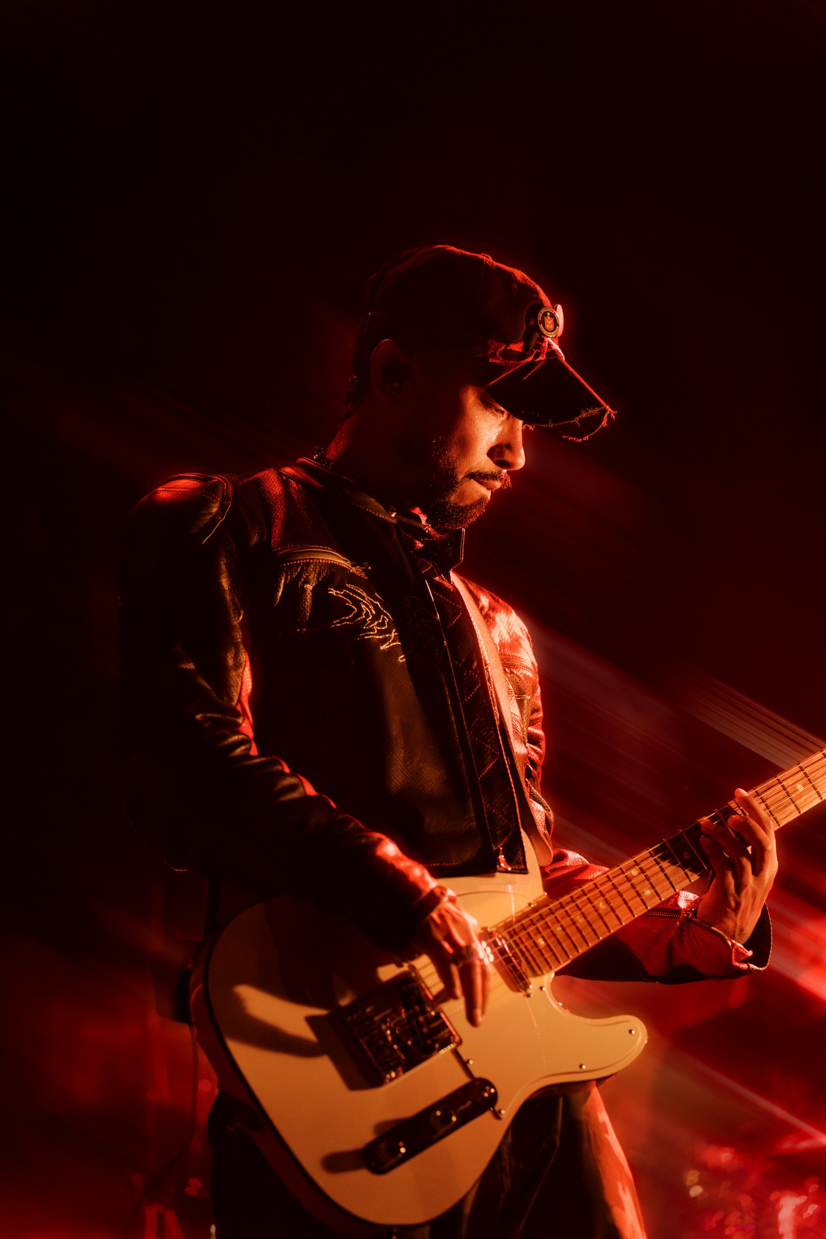 Guitarist playing electric guitar on stage with dramatic red lighting.