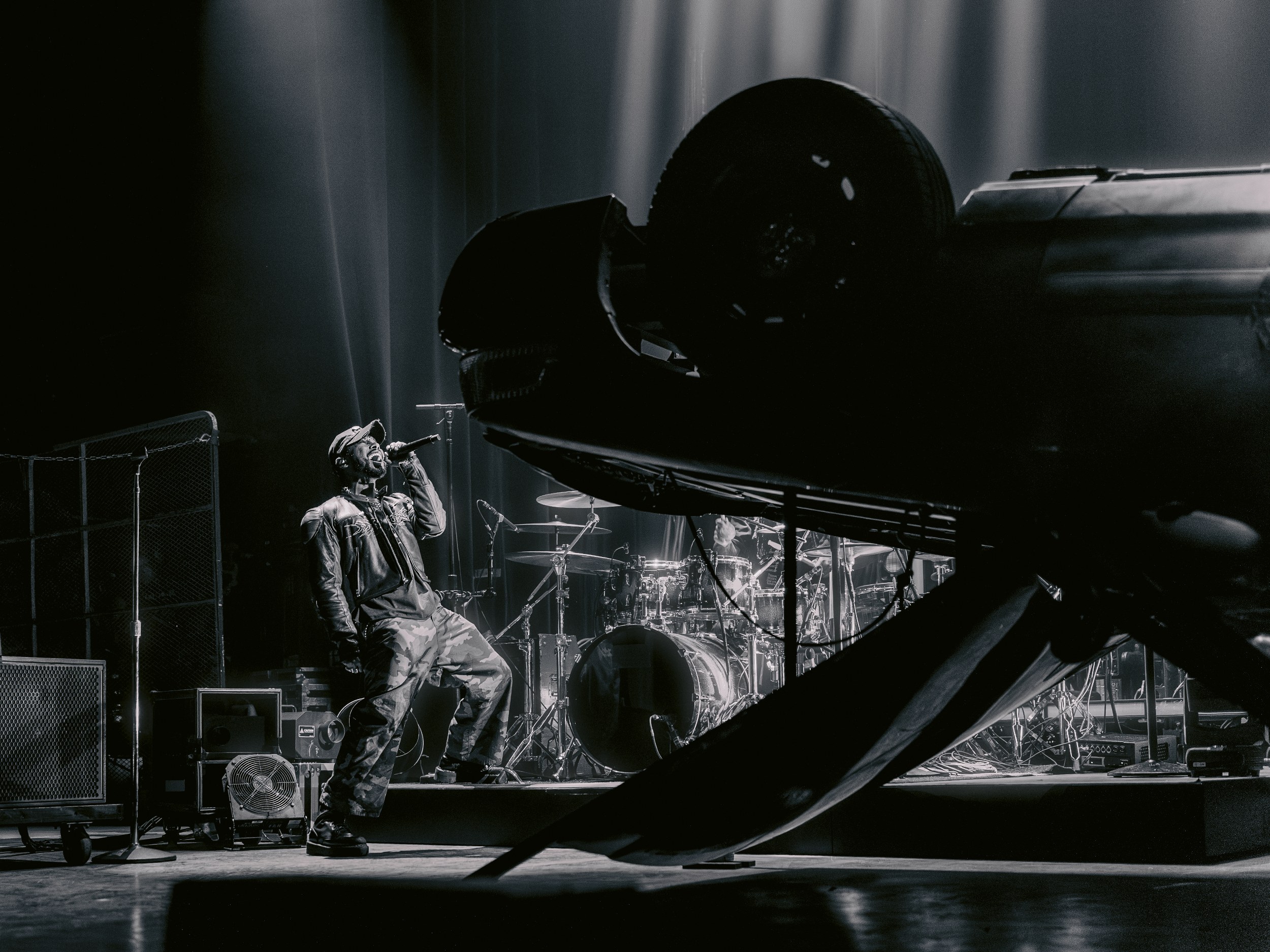 Live concert performance with singer beside an overturned car on stage.