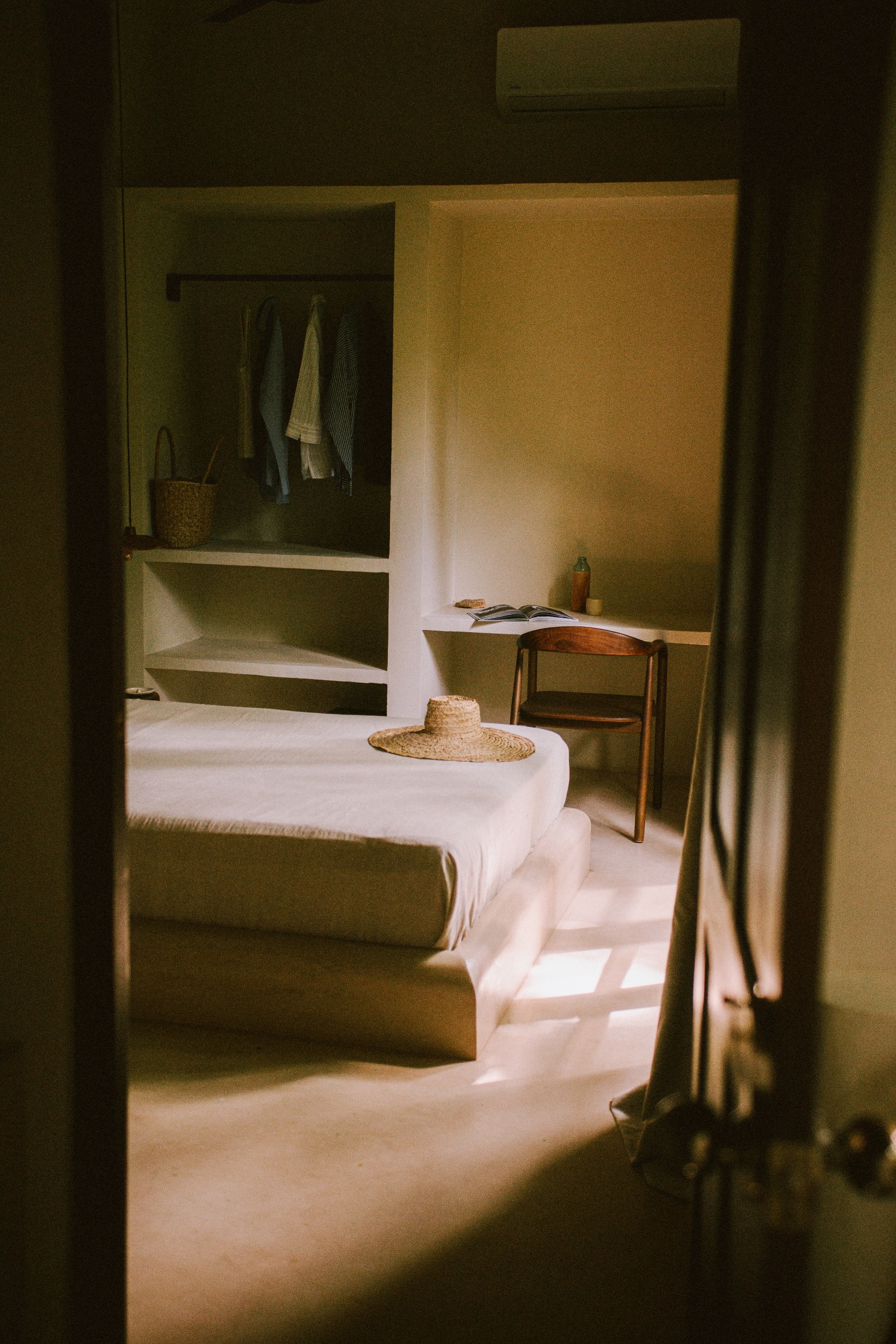 Cozy minimalist bedroom with a straw hat on the bed, soft natural lighting.