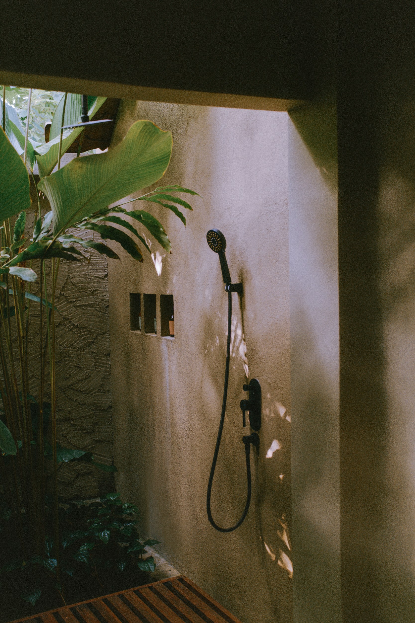 Outdoor shower with tropical plants and wooden floor in natural light.