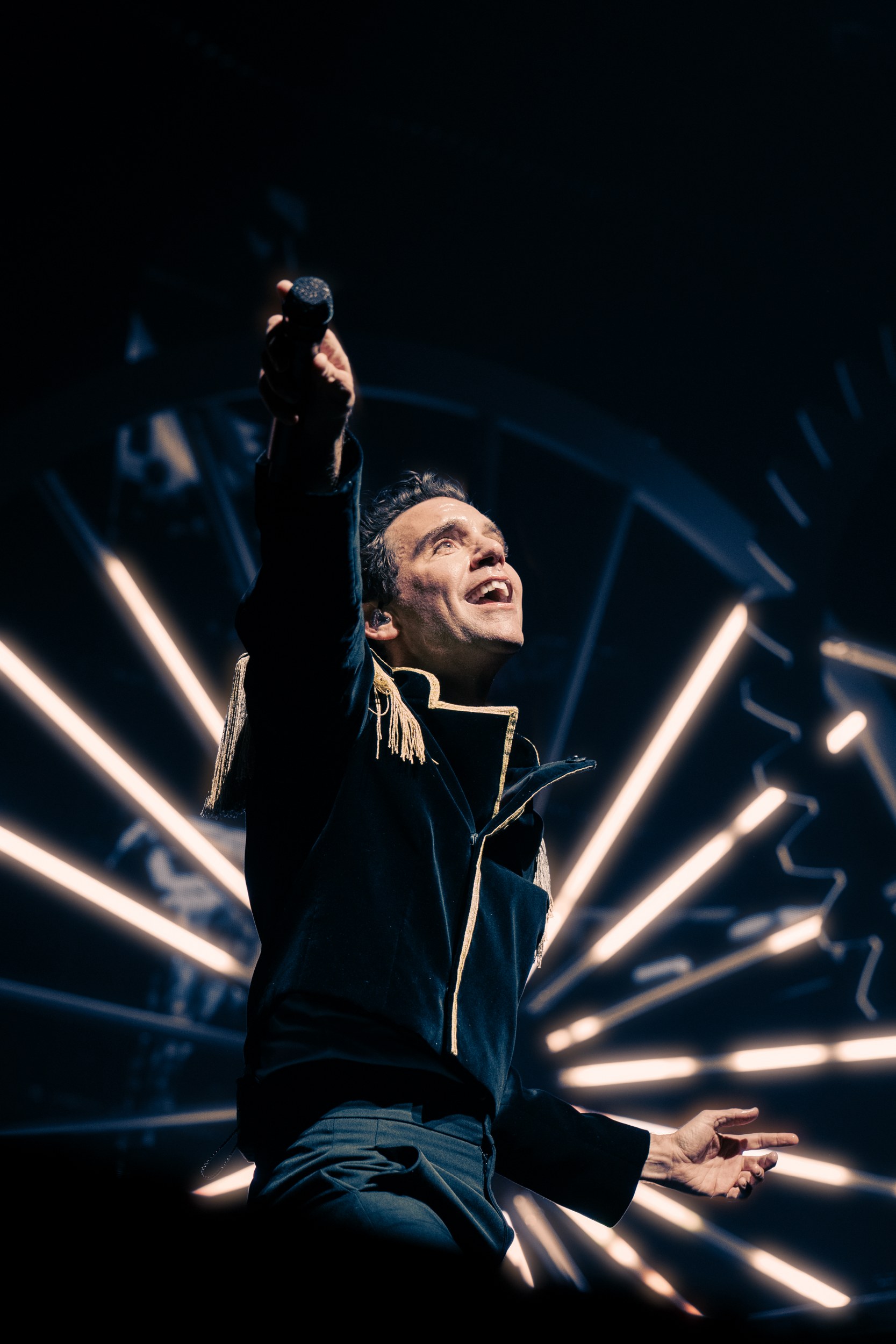 Performer singing on stage with dramatic lighting in the background.