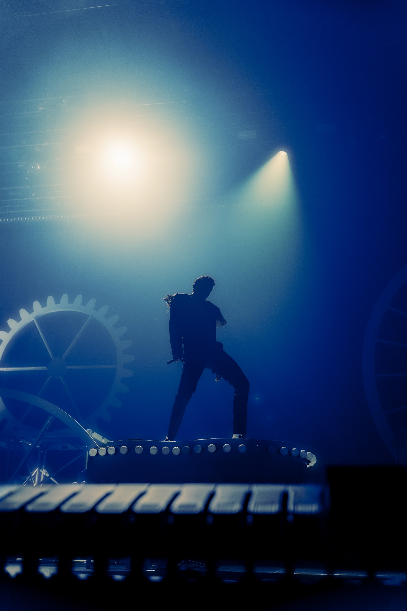 Performer on stage in dramatic lighting with gear decoration.