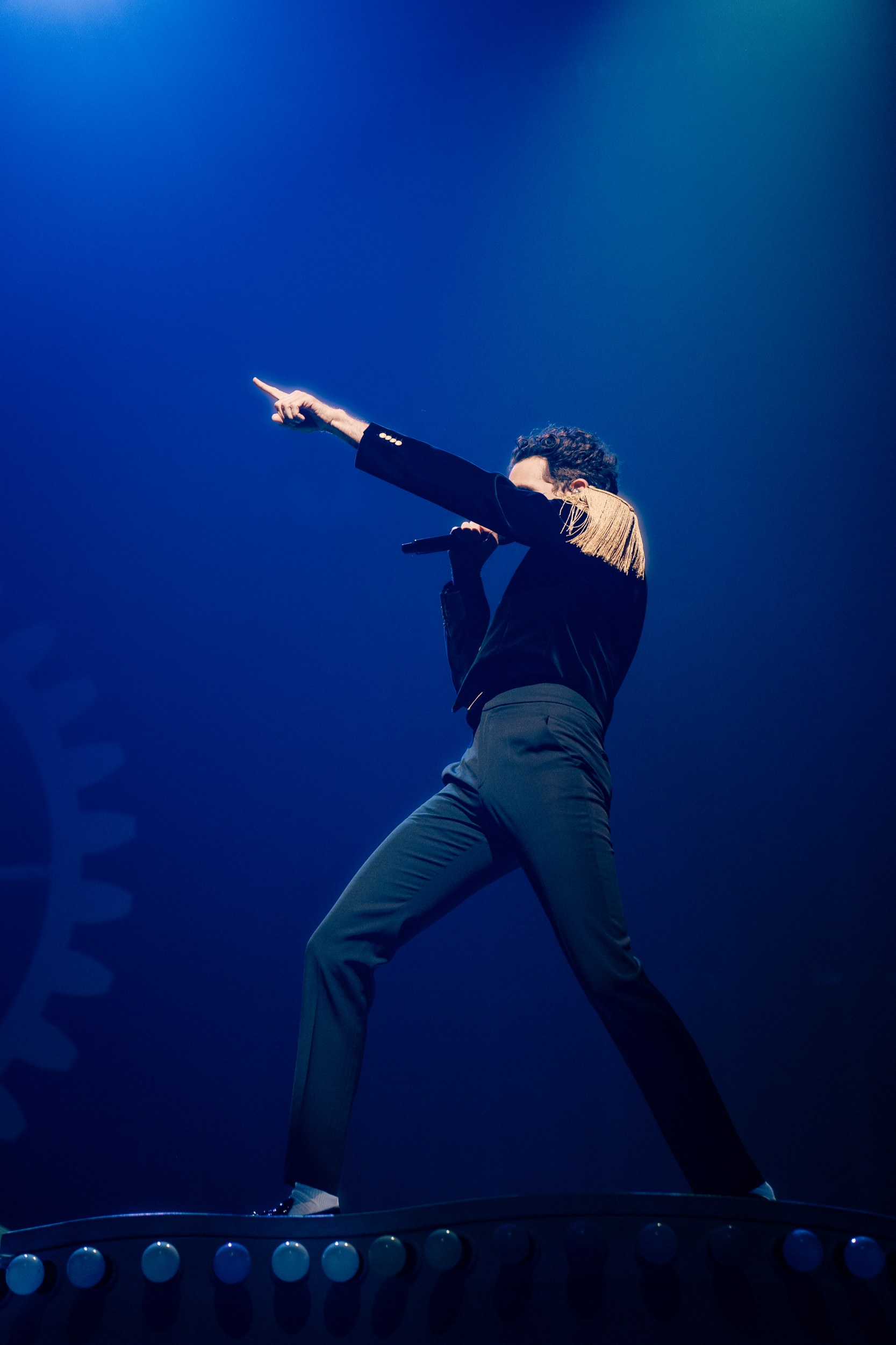 Performer on stage striking pose under blue spotlight.