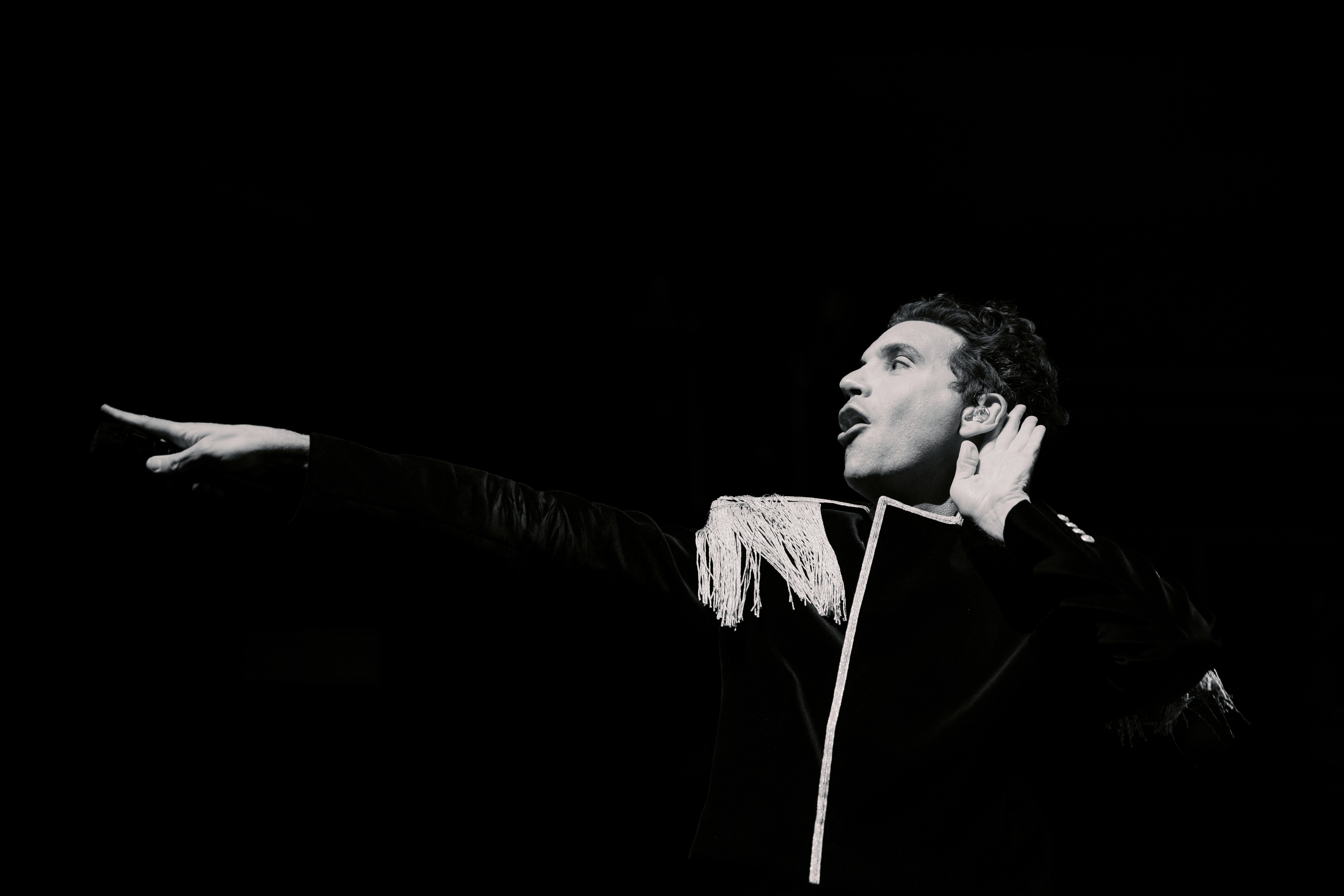 Performer in black outfit gestures dramatically on stage.