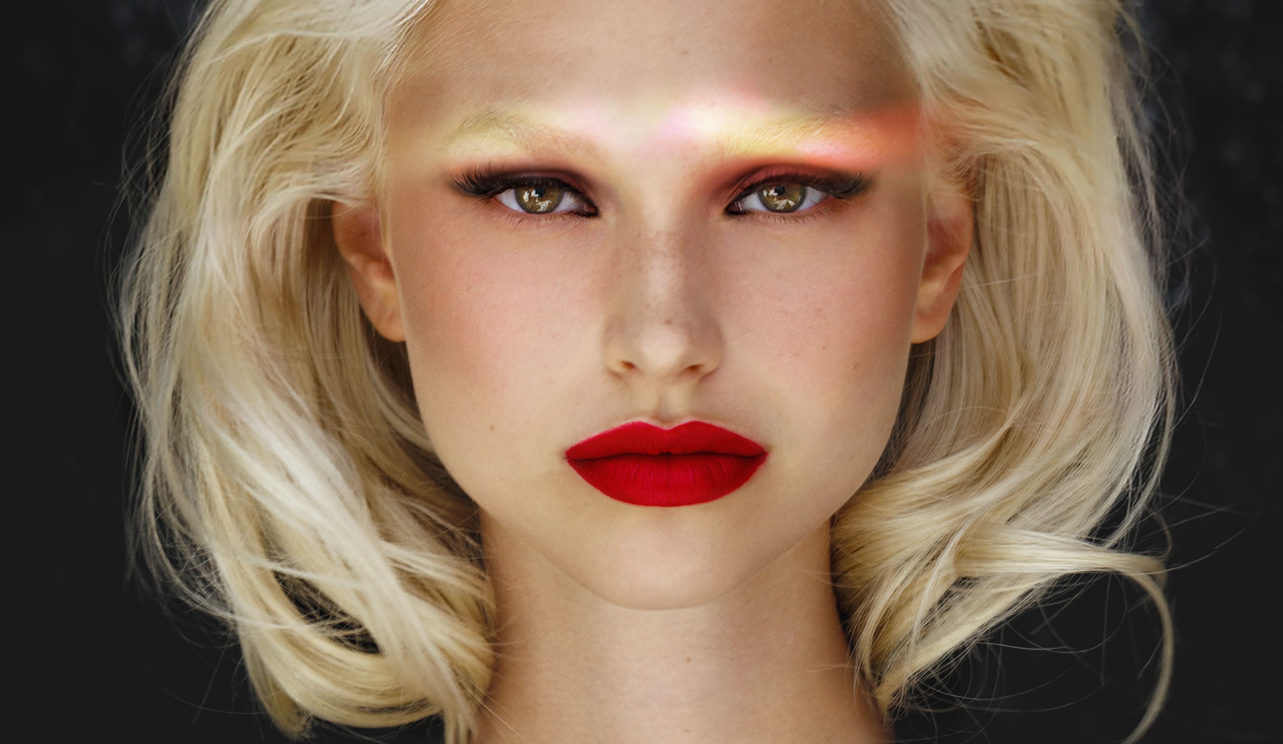 Model with bold red lipstick and blonde hair, dramatic lighting effect on face.