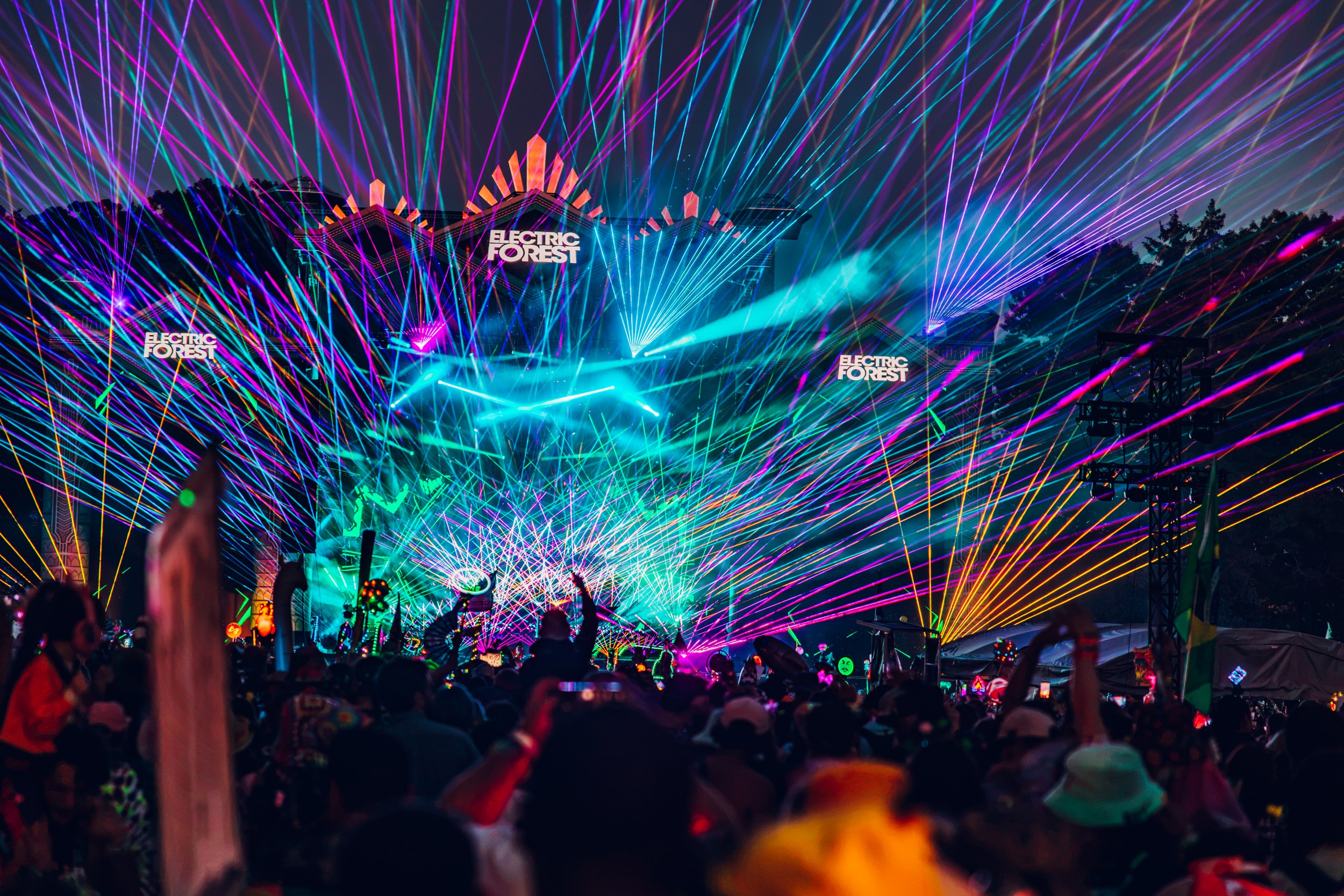 Colorful laser lights and crowd at a vibrant music festival at night.