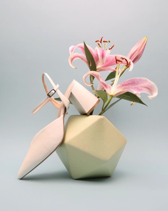 Elegant shoe with pink lilies in a modern vase on soft blue background.