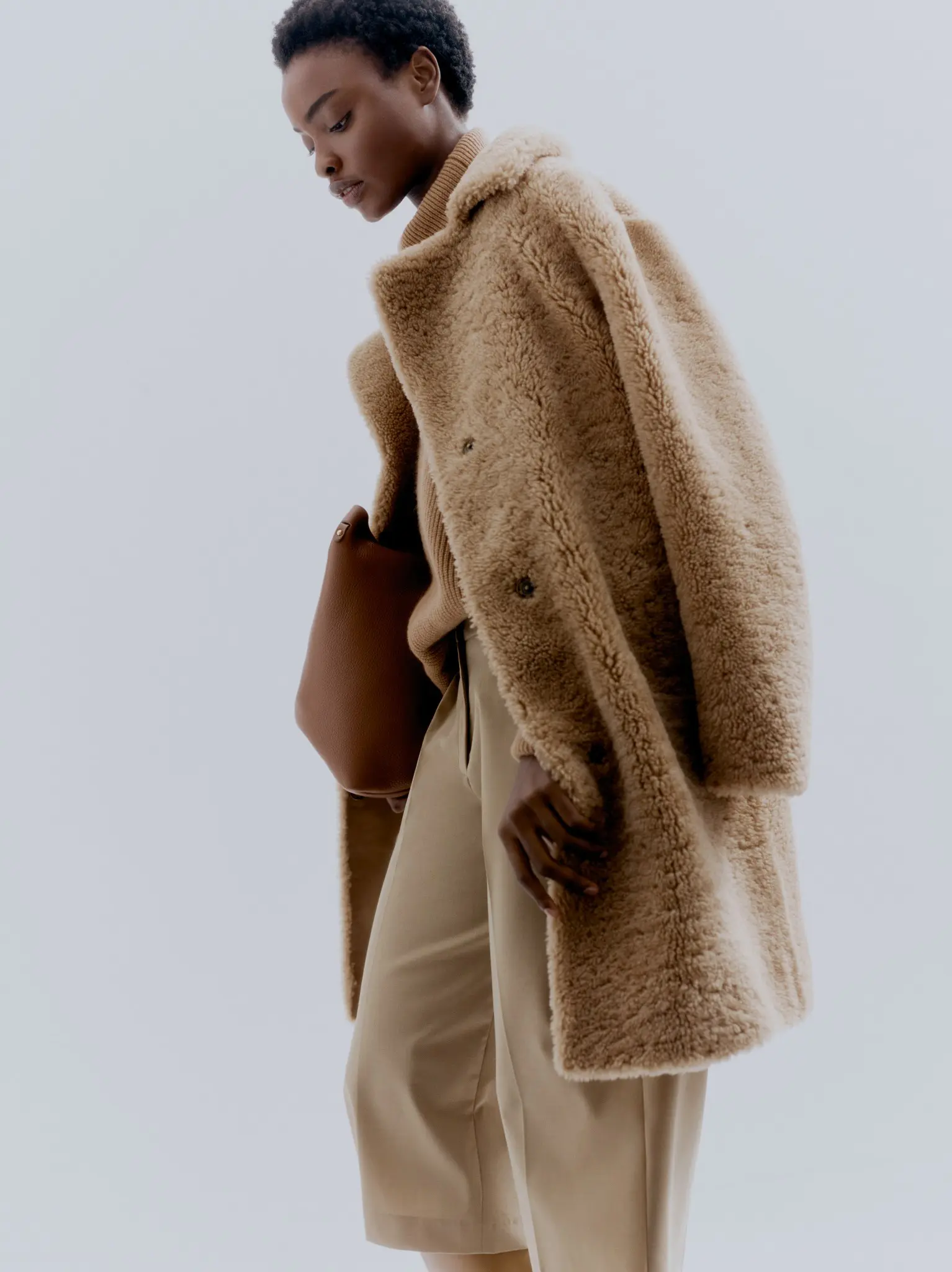 Model in chic beige coat and trousers, holding a brown bag, styled for autumn fashion.