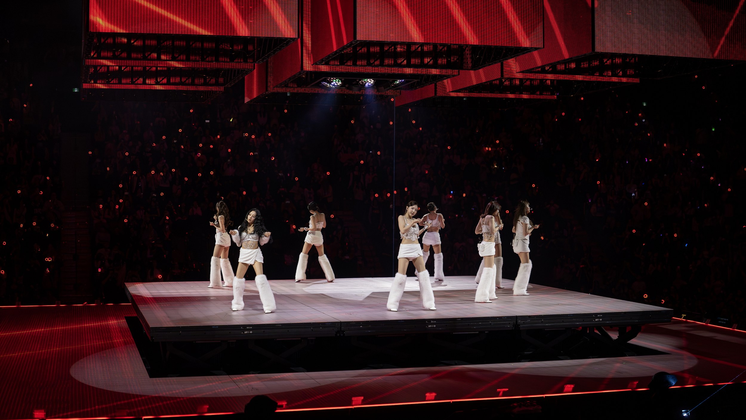 K-pop group performs live on stage under vibrant red lights.