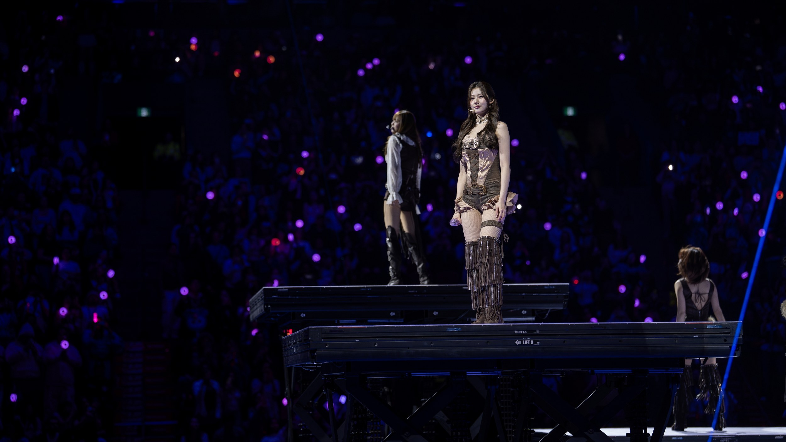 Performers on stage in front of a vibrant, glowing crowd.