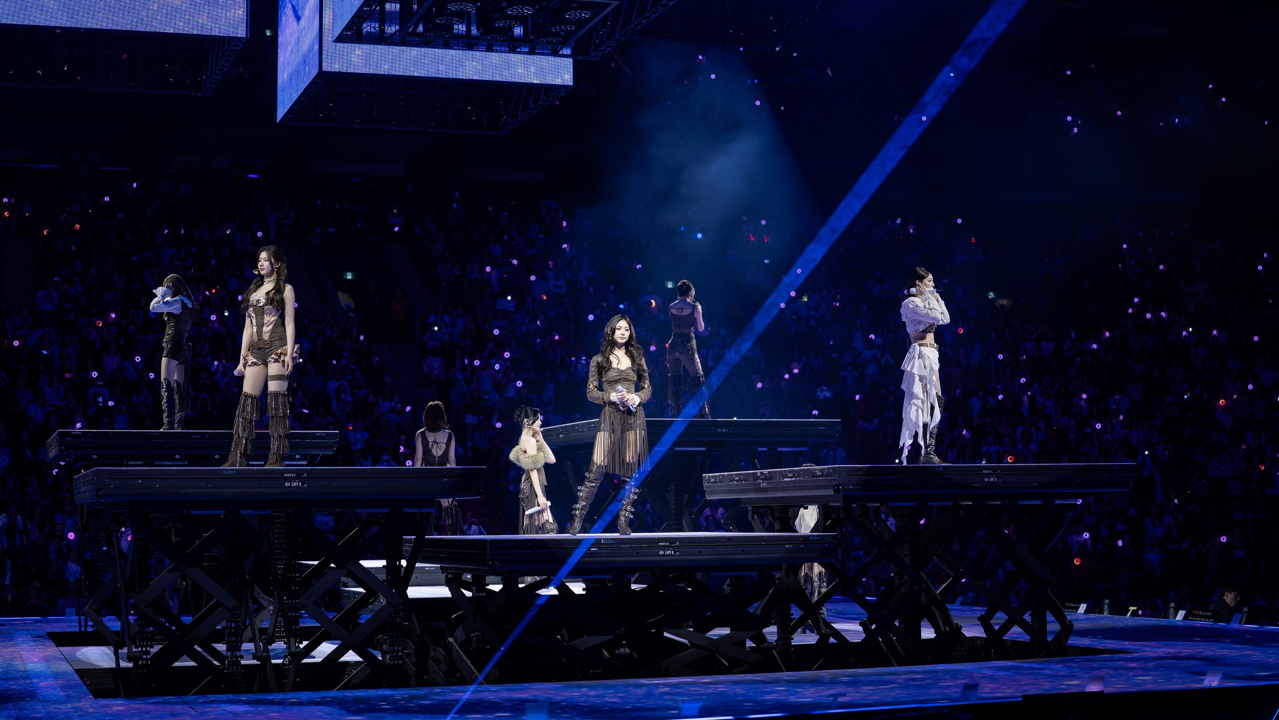 K-pop group performing live on stage with vibrant lighting effects.