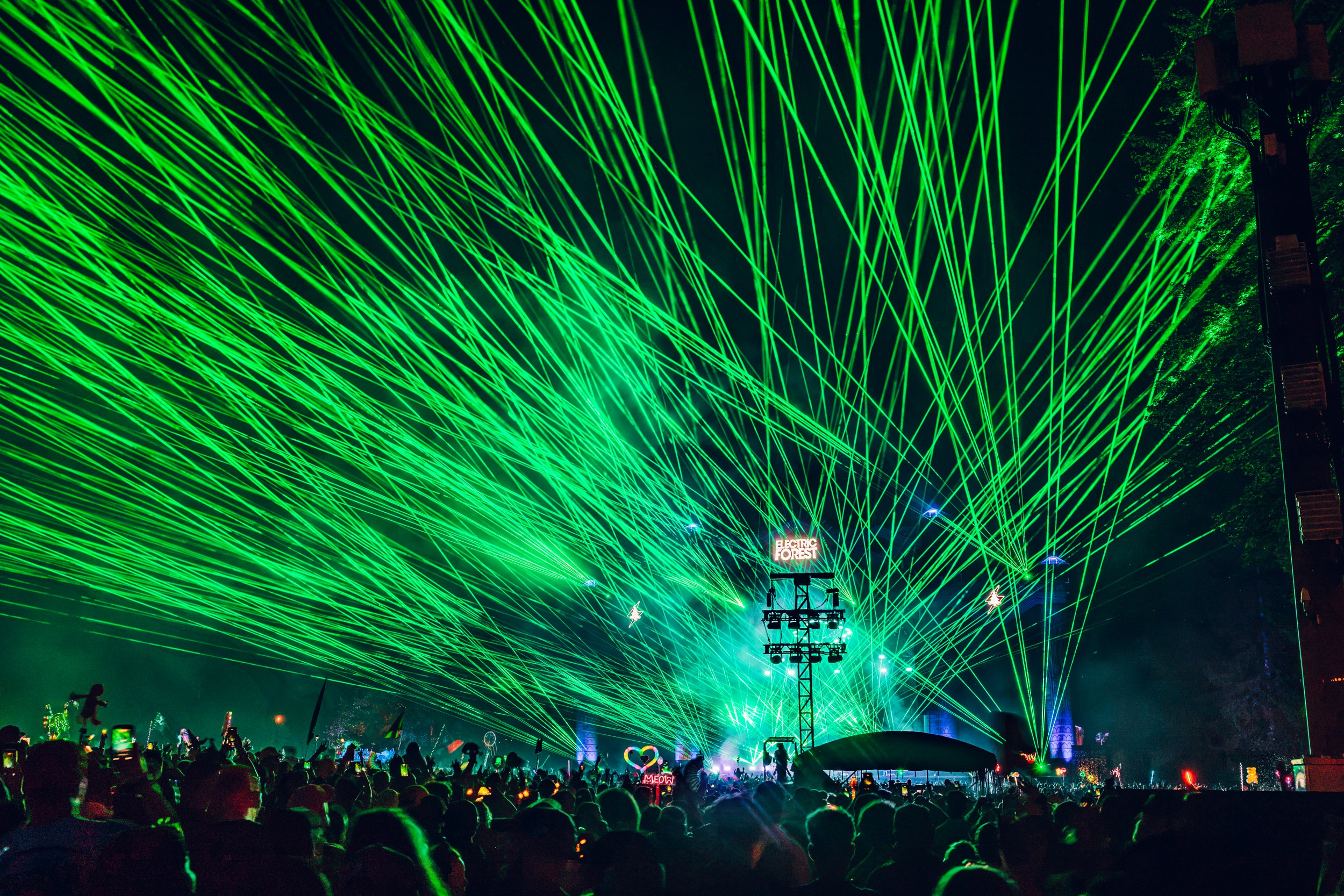 Vibrant green laser show at a crowded outdoor music festival at night.