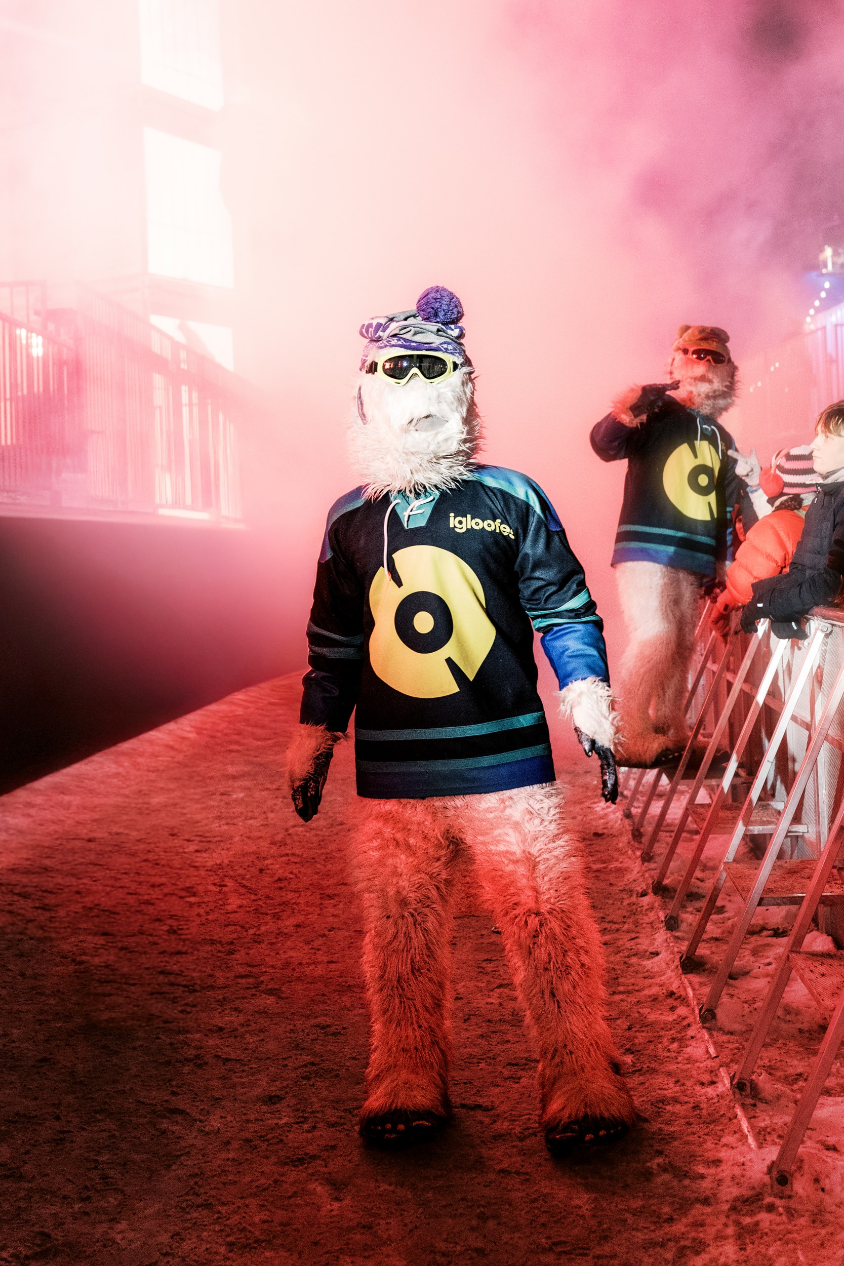 Furry costumed creatures at a winter festival with colorful lights and fog.