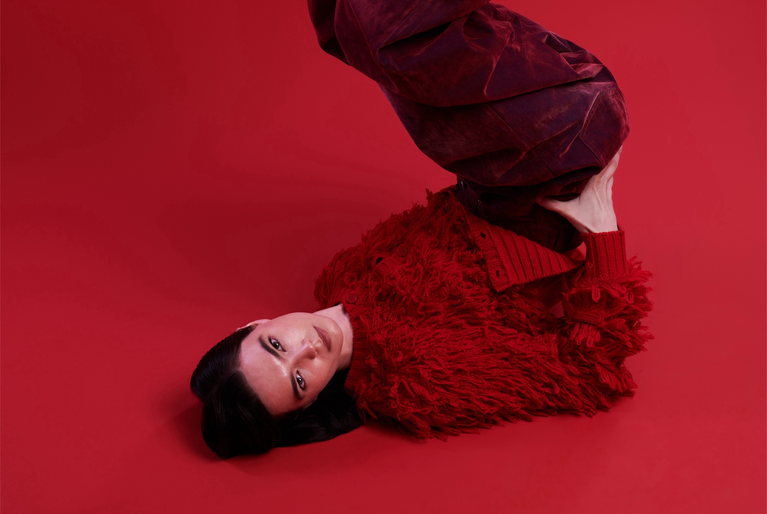 Person in a textured red outfit against a red background, posing creatively.