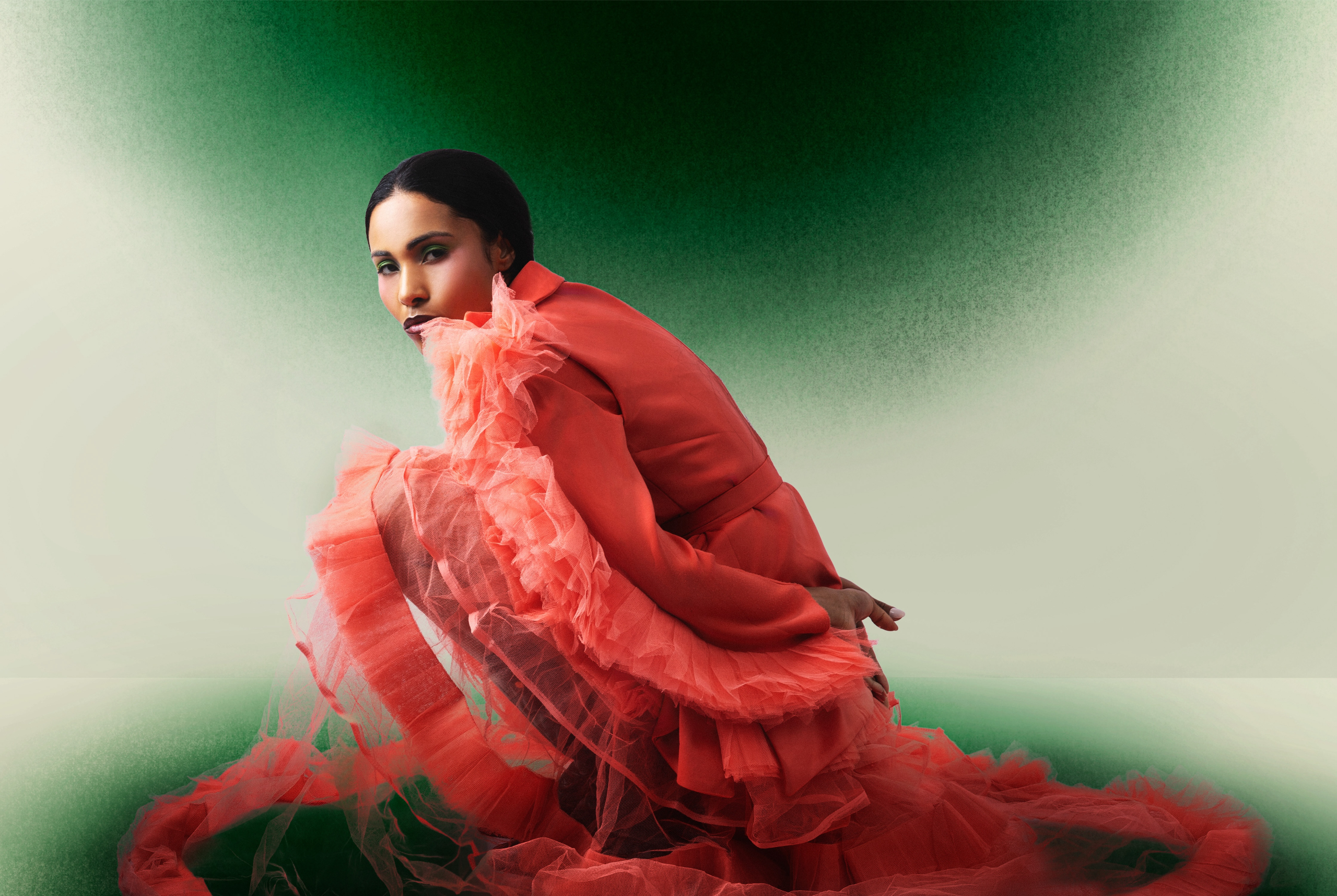 Woman in flowing coral dress poses against a green gradient background.