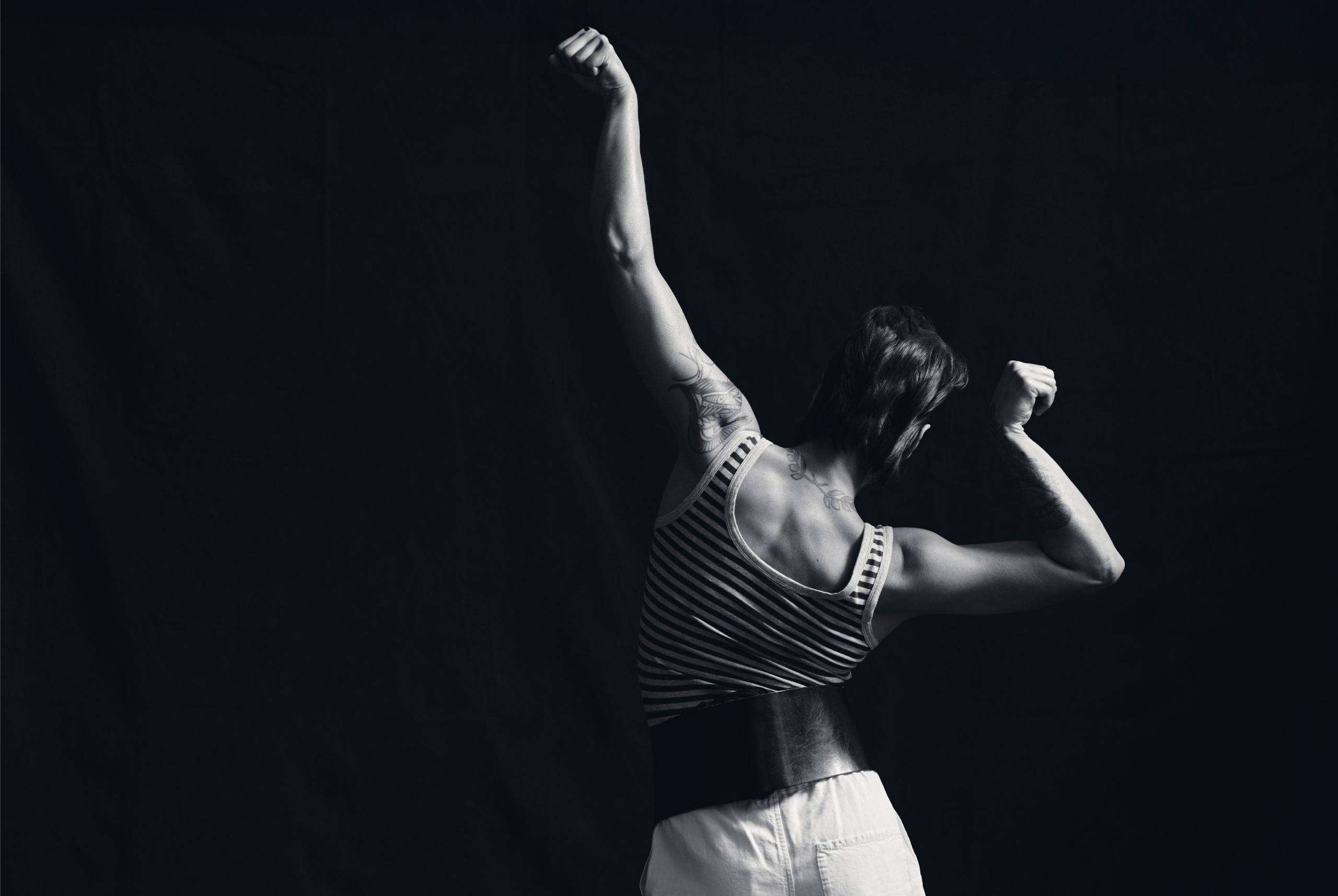 Person flexing muscles in striped tank top against dark background.