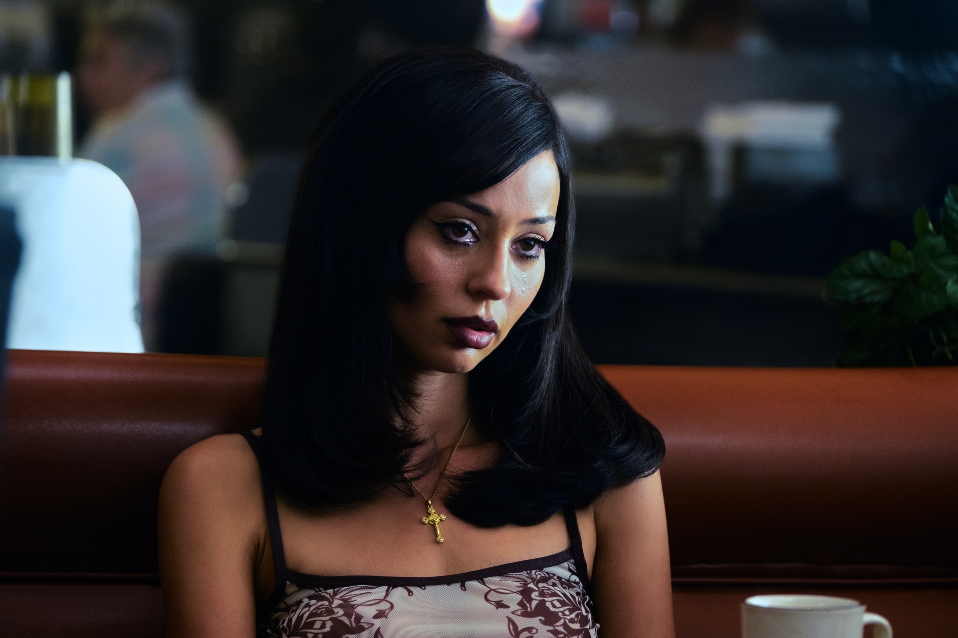 Woman with long dark hair in a diner booth, wearing a cross necklace.