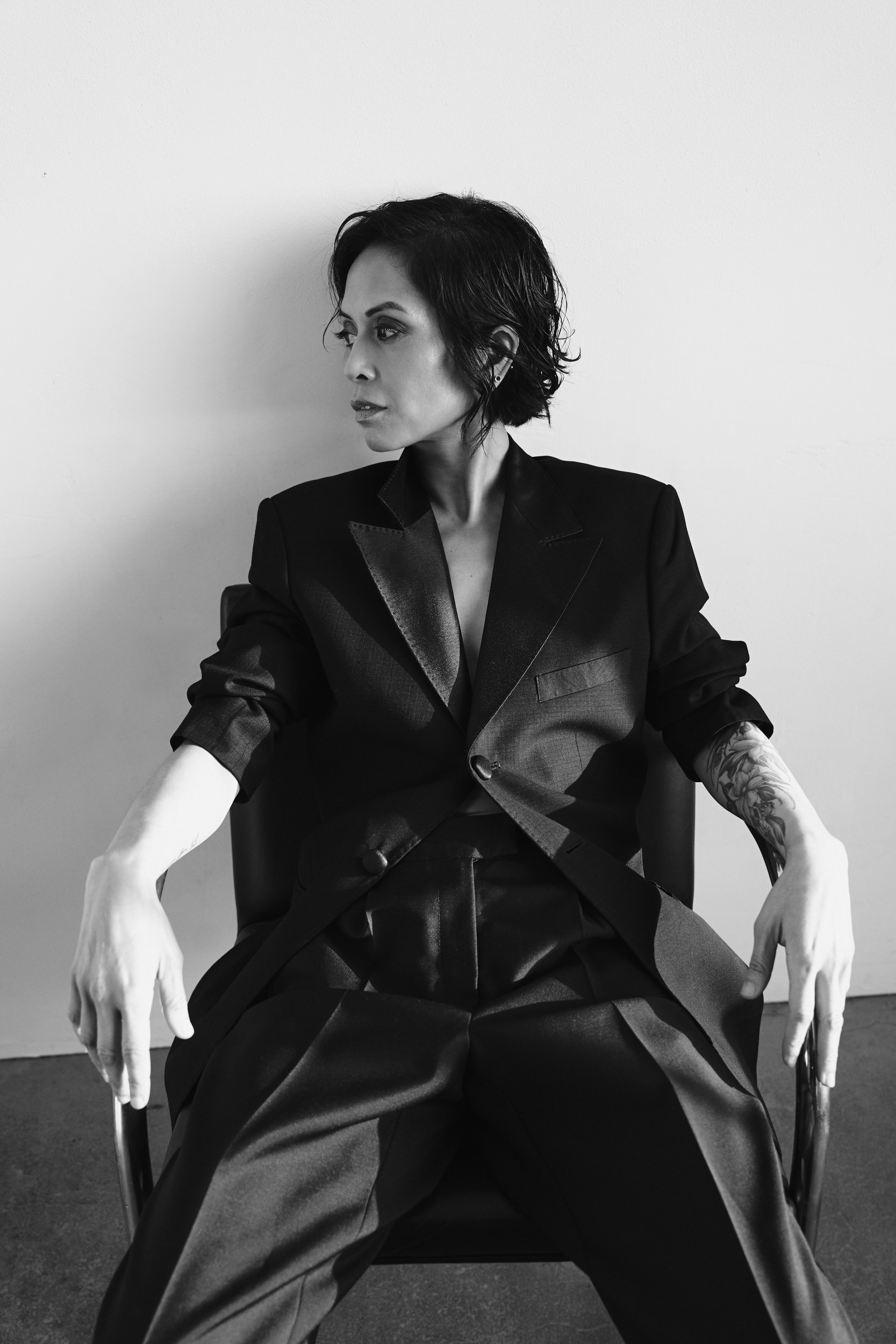 Stylish person in a black suit sitting confidently against a white background.