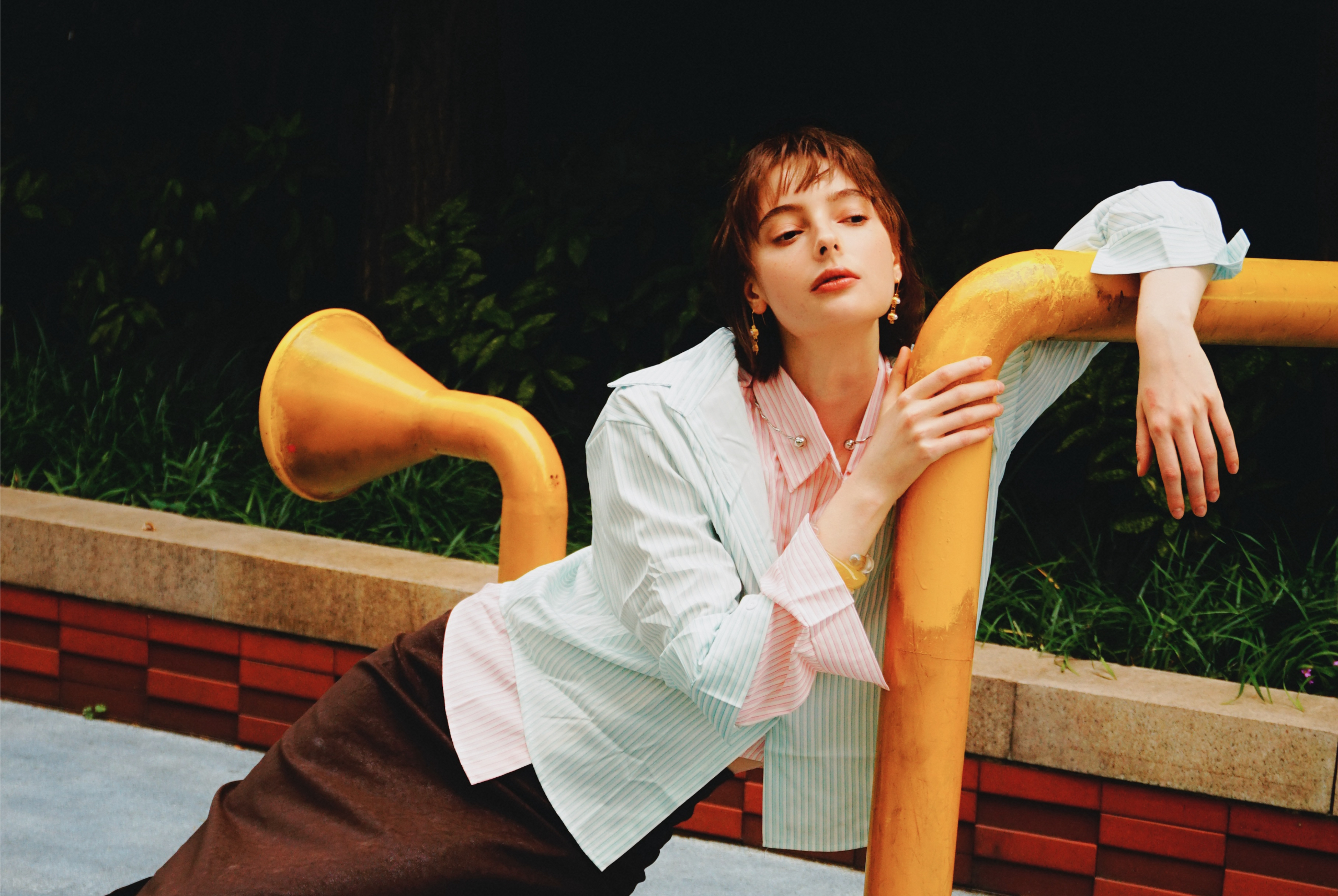 Fashionable woman in striped shirt posing on yellow structure outdoors.