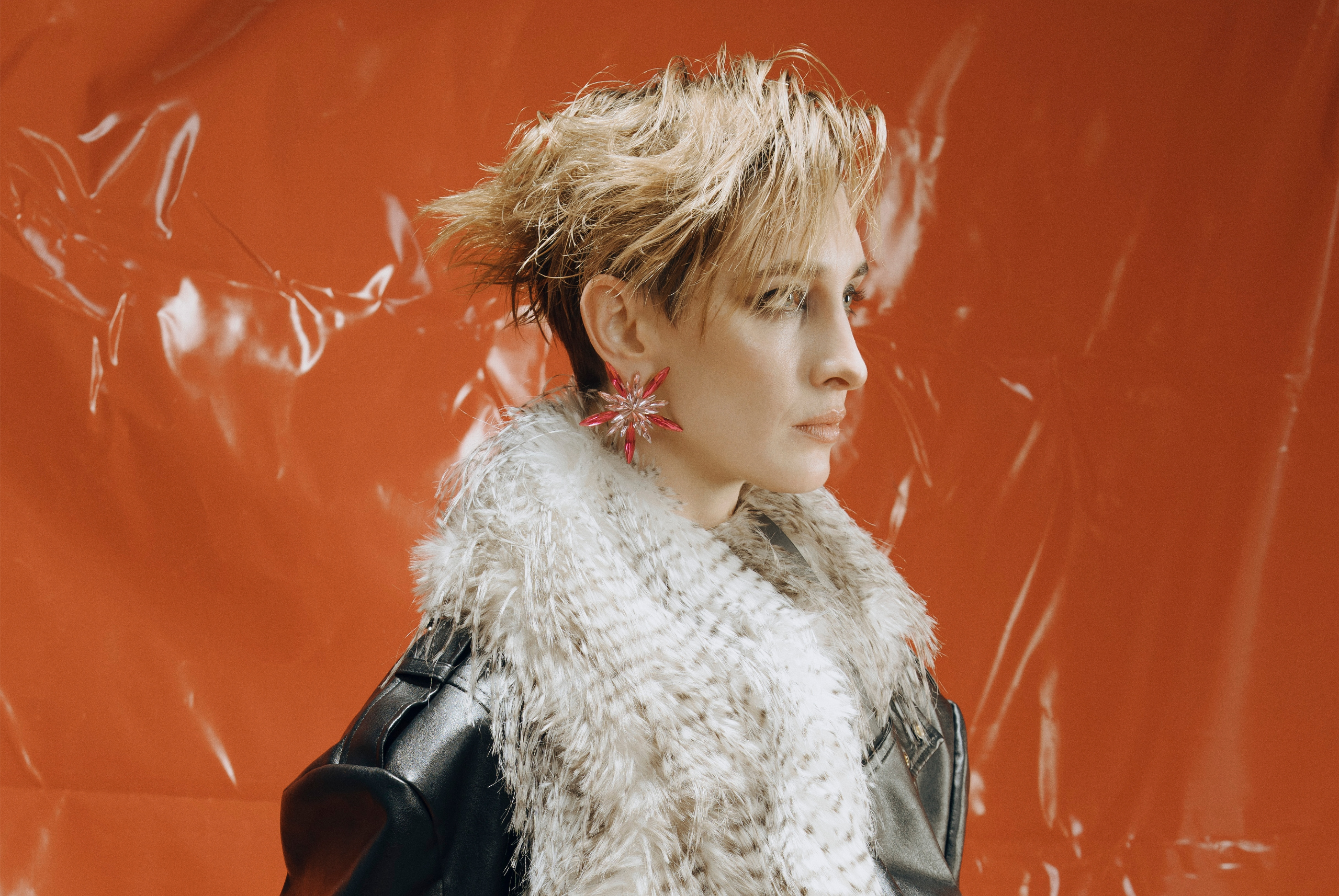 Fashion model with edgy hairstyle and fur coat against vivid orange background.