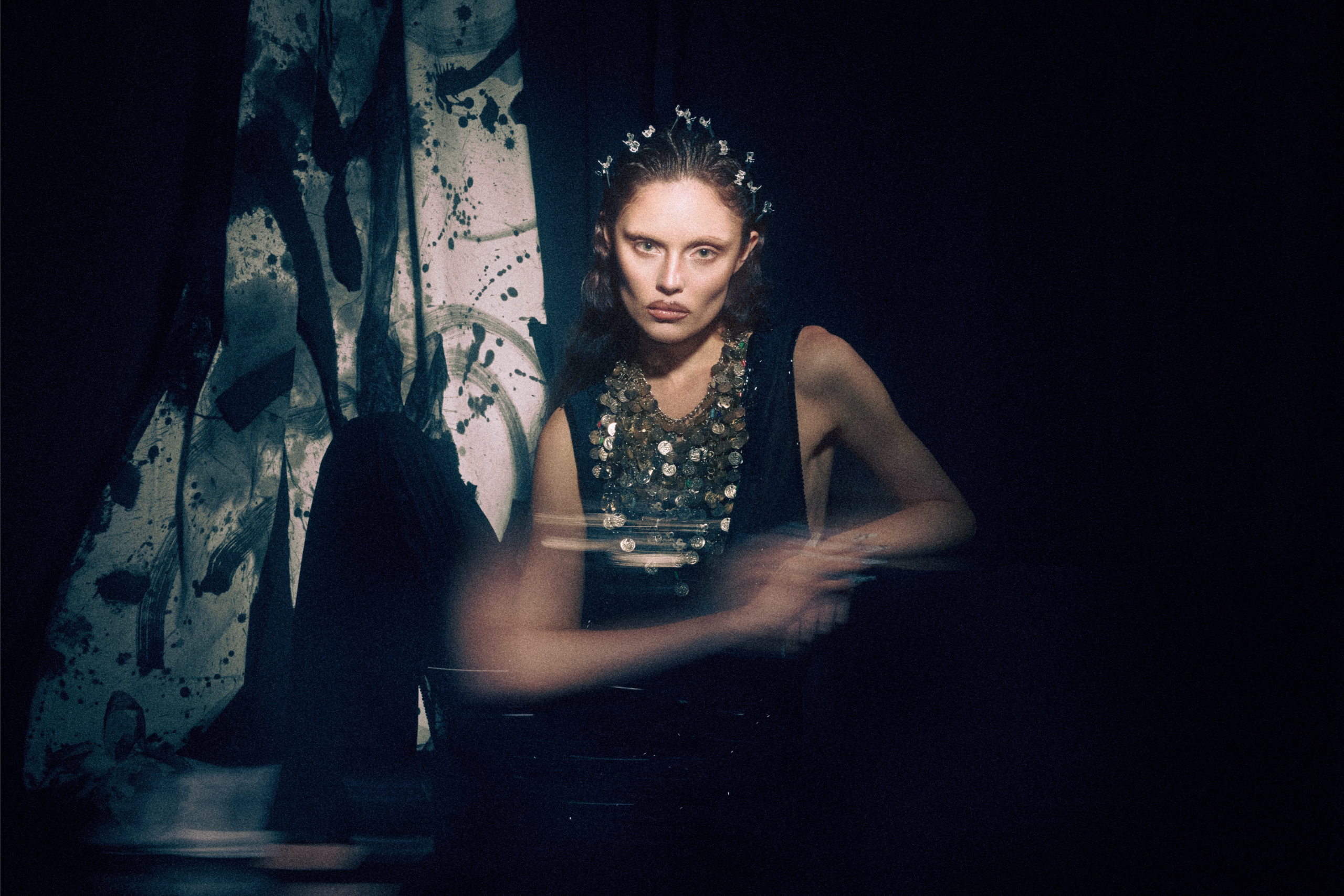Elegant woman in dark sequin dress with artistic backdrop, dramatic lighting.