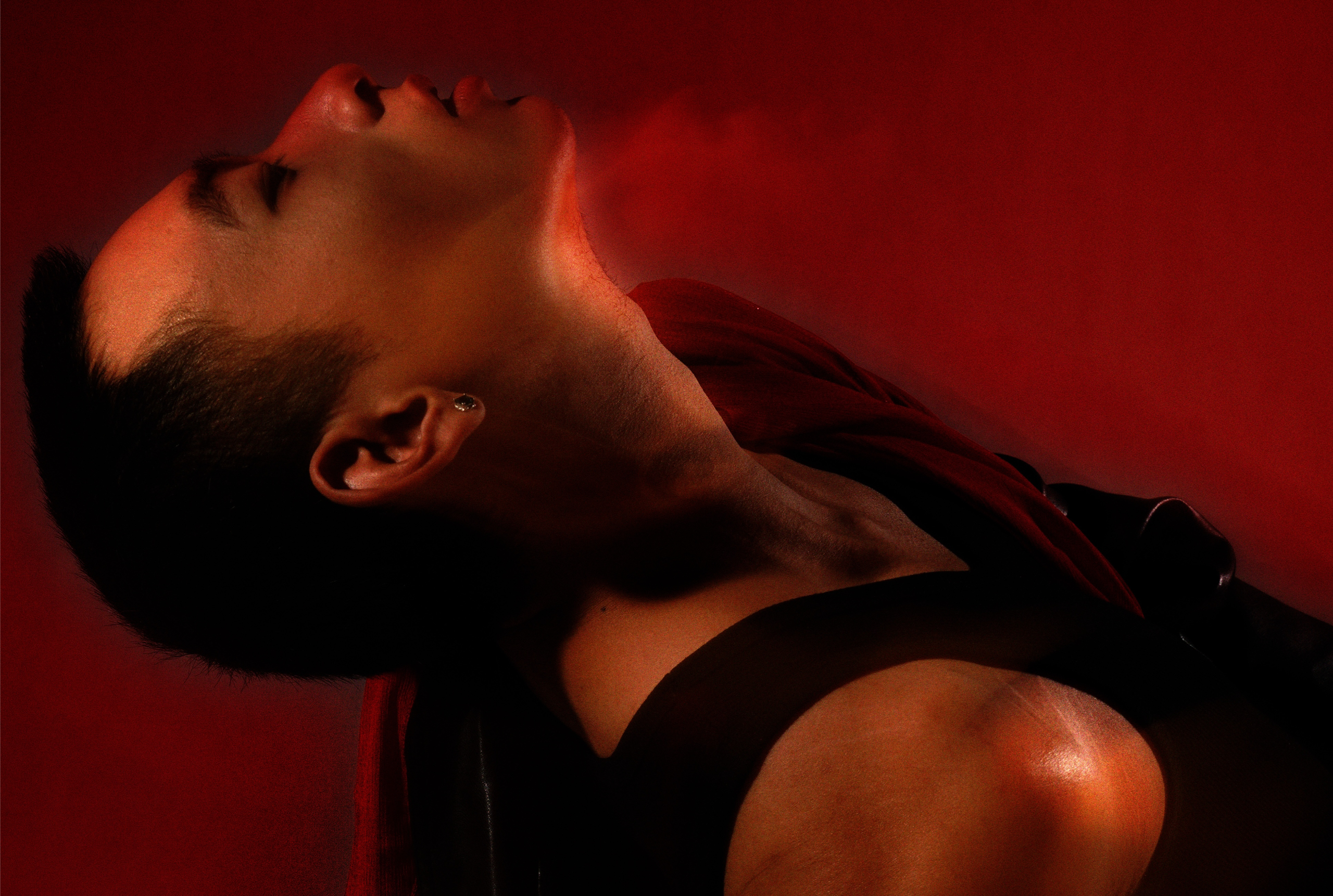Dramatic portrait in red lighting showing serene expression and neck lines.