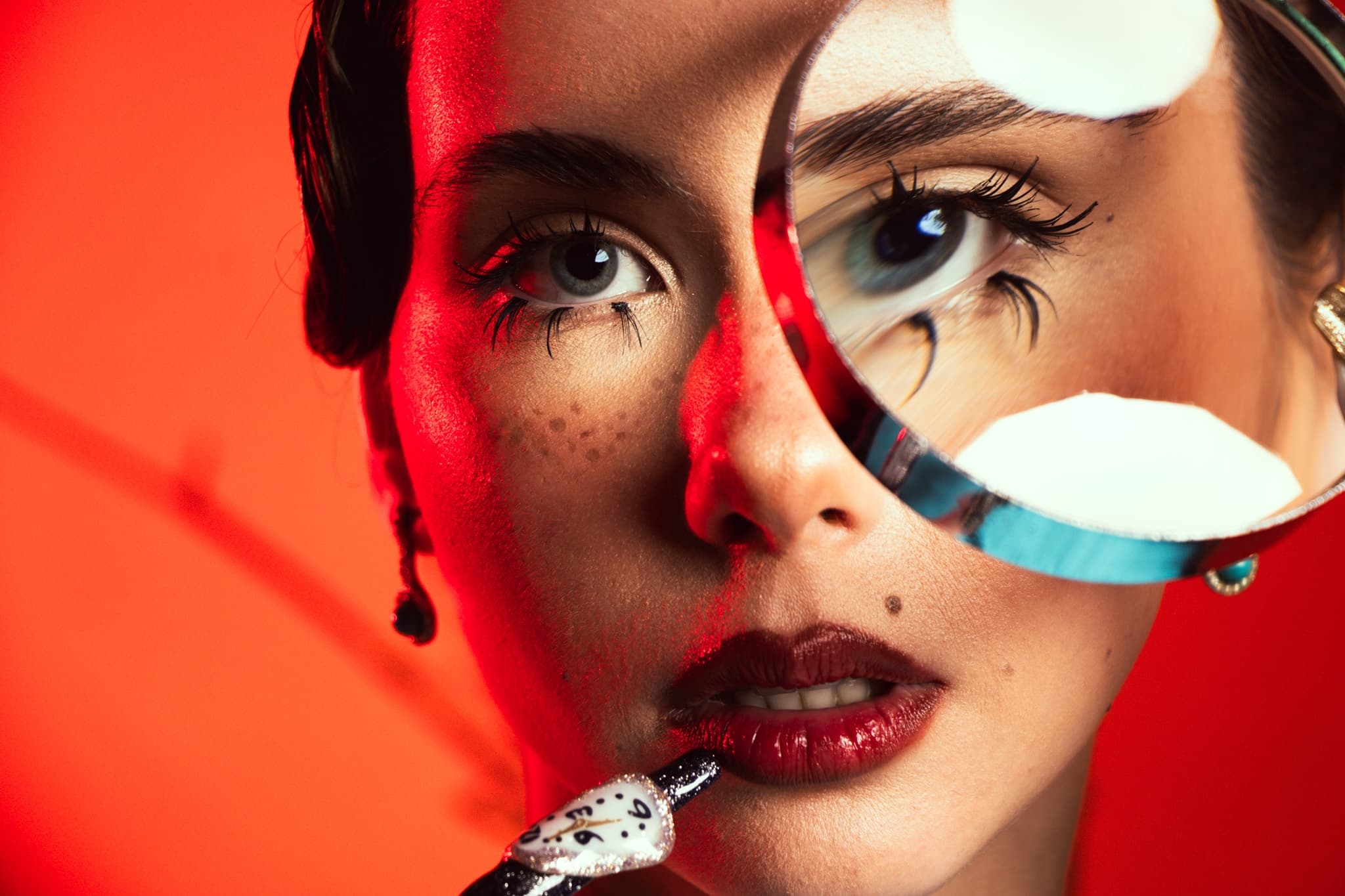 Artistic close-up of a woman's face with red lighting and magnifying glass effect.